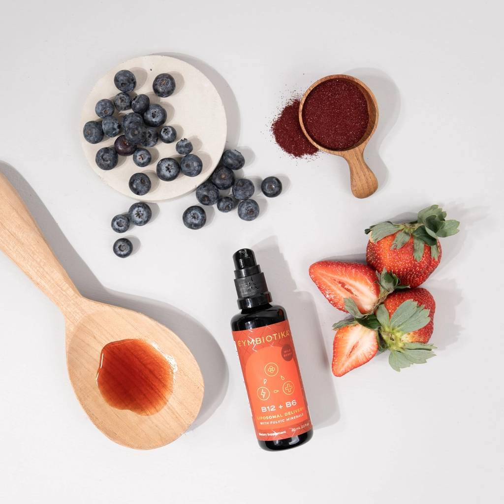 Cymbiotika Liposomal Vitamin B12 + B6 bottle with strawberries, blueberries, red powder, and a wooden spoon.
