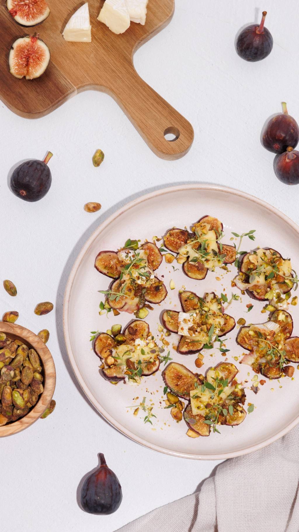 Plate of baked fig and brie bites topped with pistachios and herbs, surrounded by fresh figs.