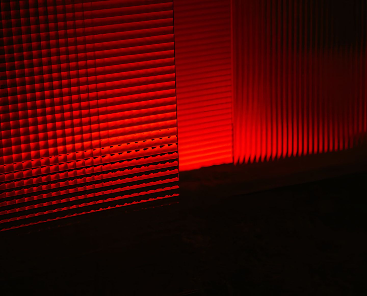 Red light casts ribbed geometric shadows across a dark surface.