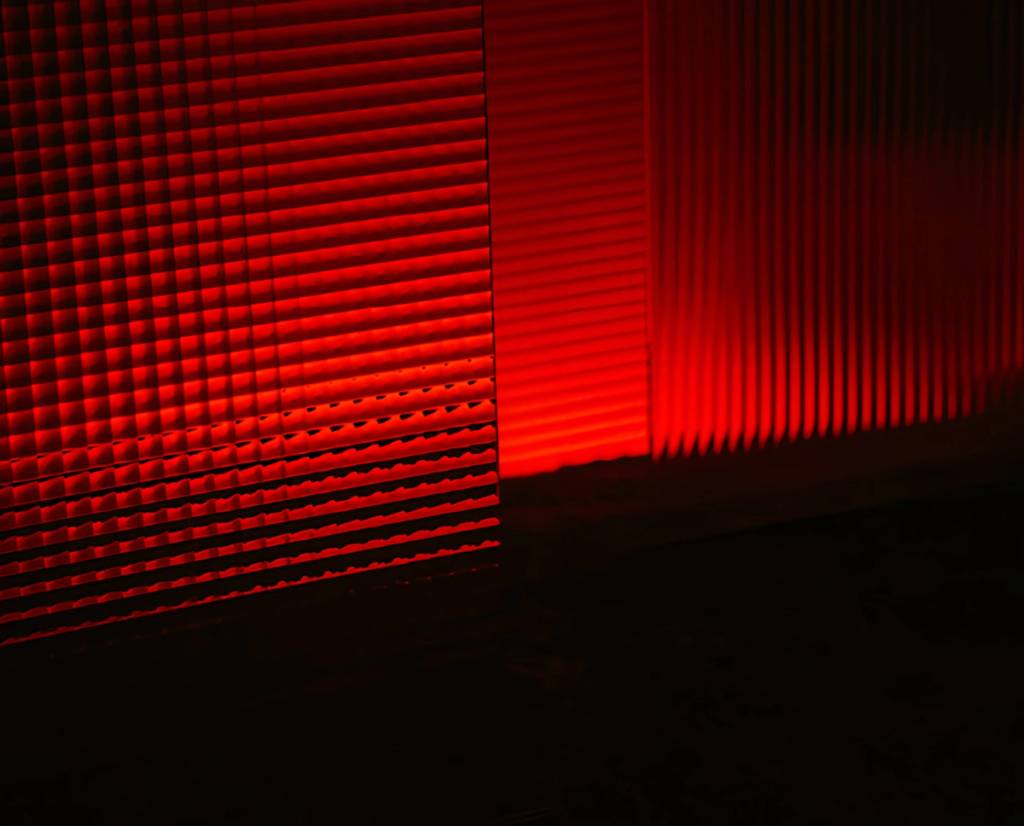 Red light casts ribbed geometric shadows across a dark surface.