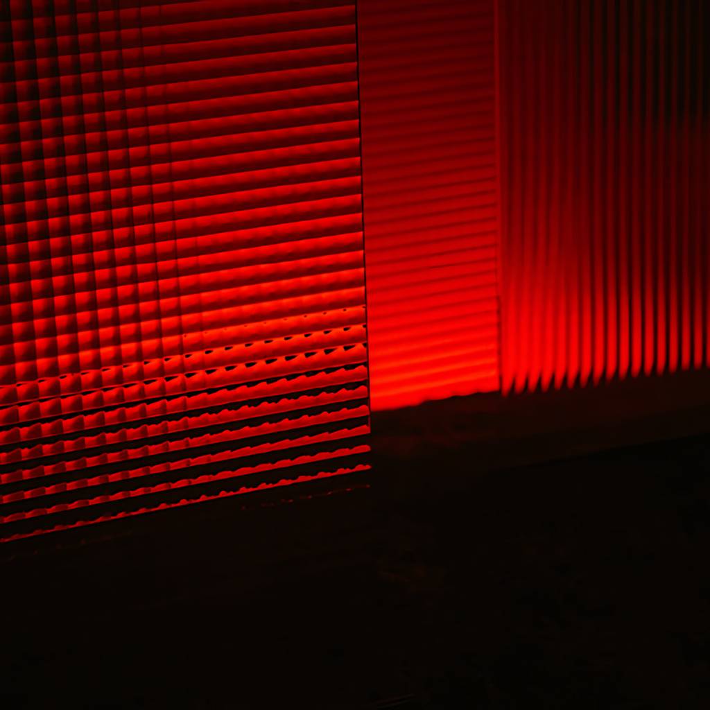 Red light casts ribbed geometric shadows across a dark surface.