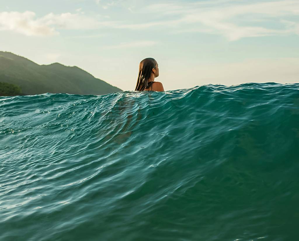 Woman with wet hair swimming in ocean waves near a mountainous shoreline