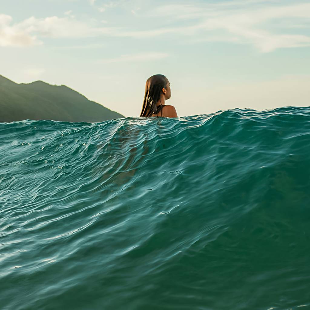 Woman with wet hair swimming in ocean waves near a mountainous shoreline
