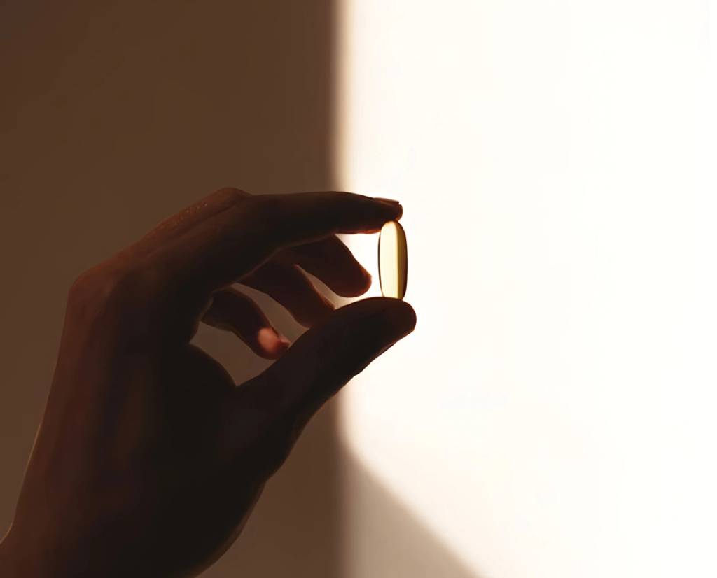 Hand holding a golden softgel capsule against warm sunlight