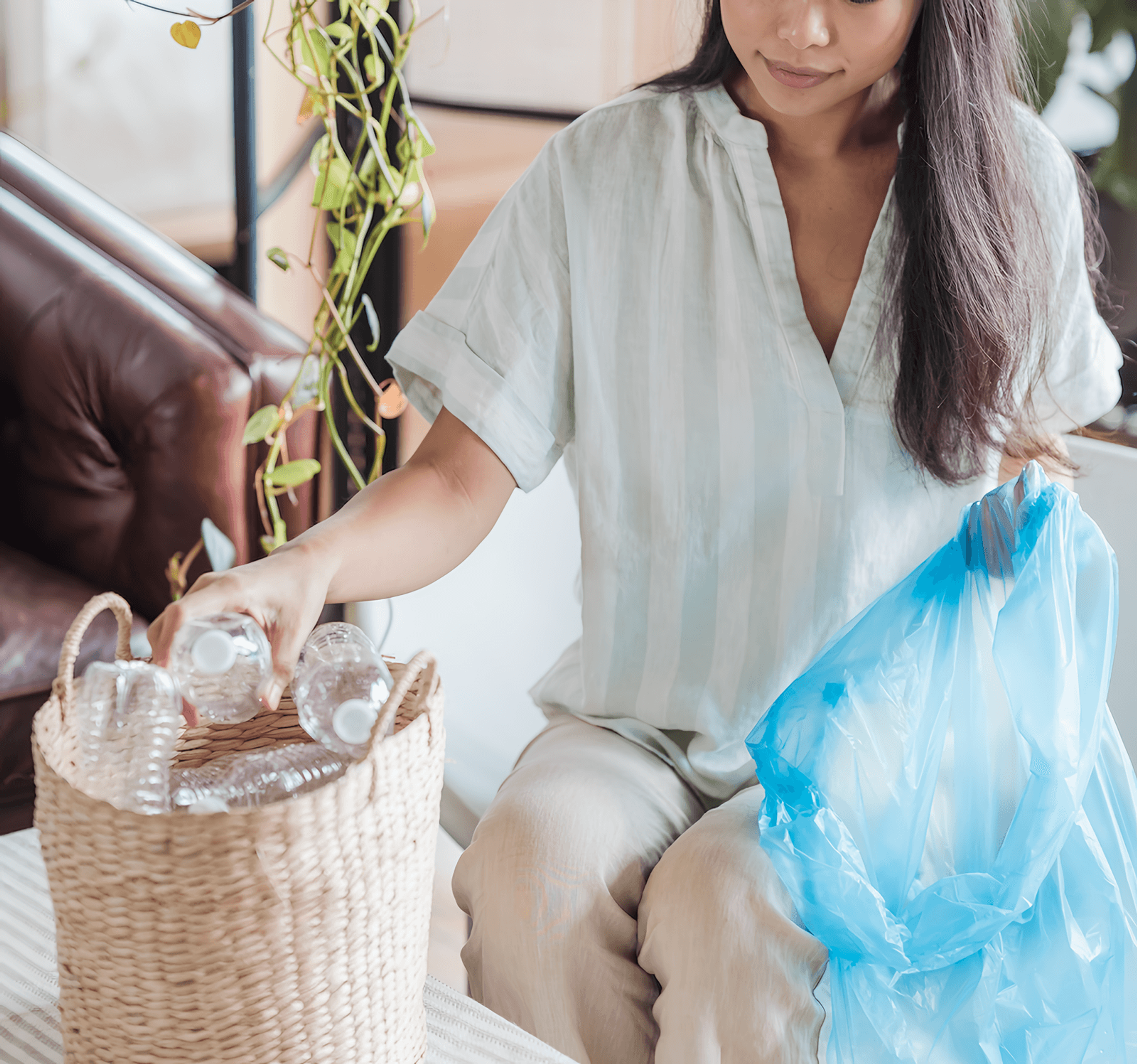 A woman places clear bottles in a woven basket beside a blue bag.
