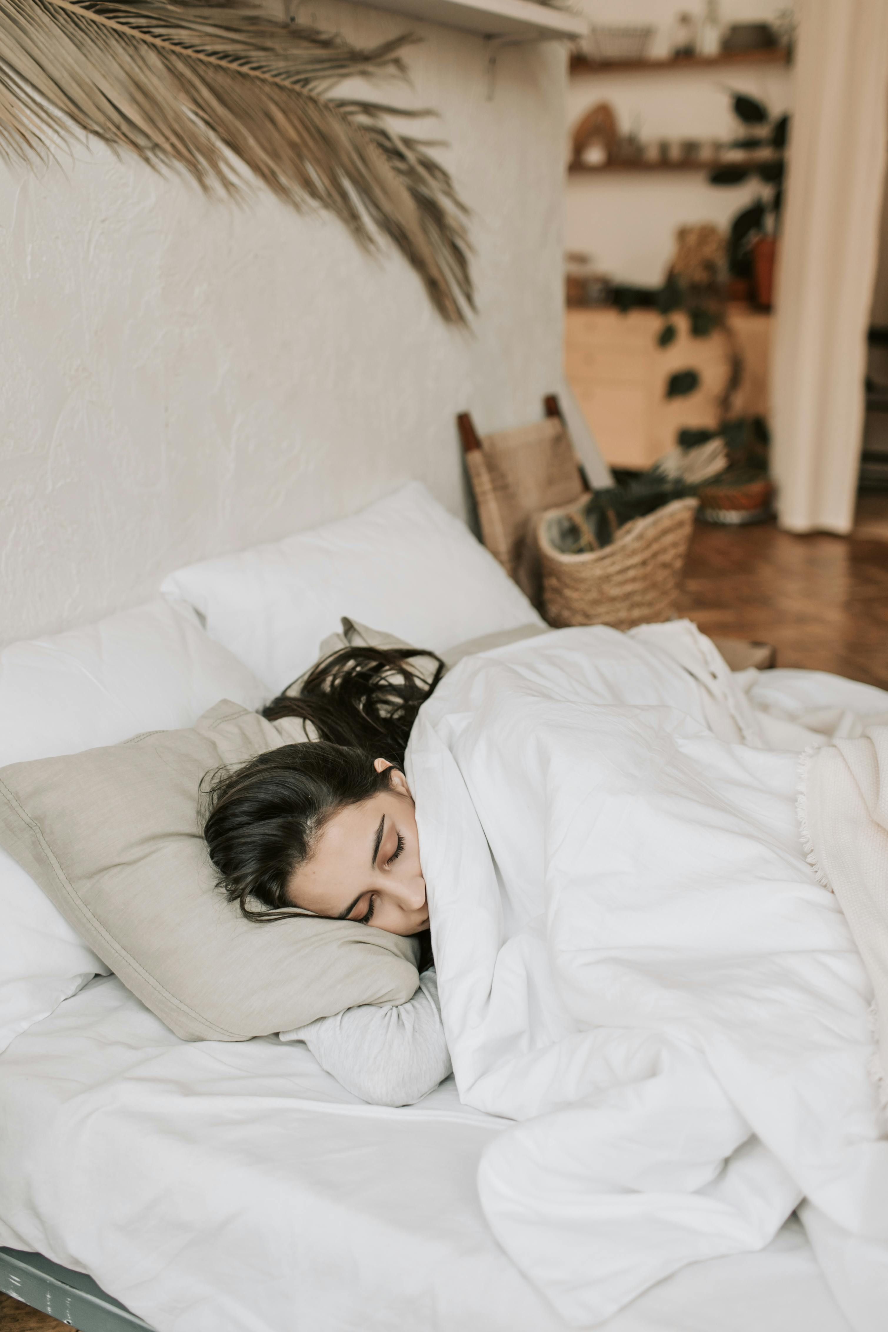 Woman sleeping on her side in a white bed under a white duvet.