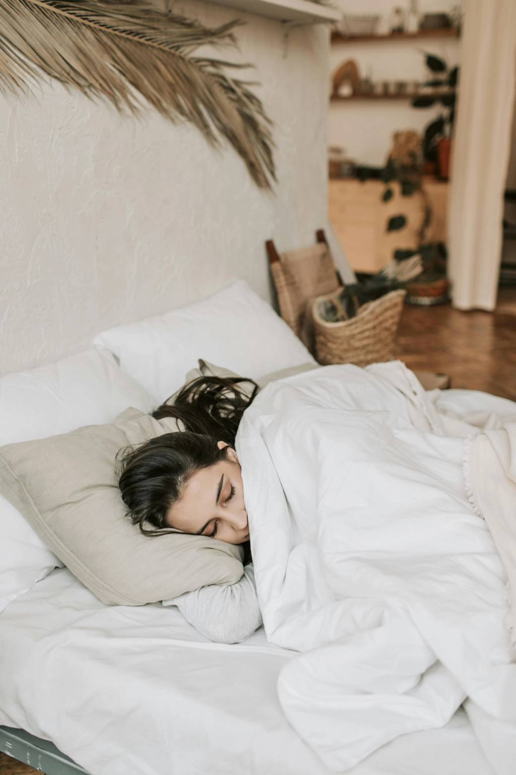 Woman sleeping on her side in a white bed under a white duvet.