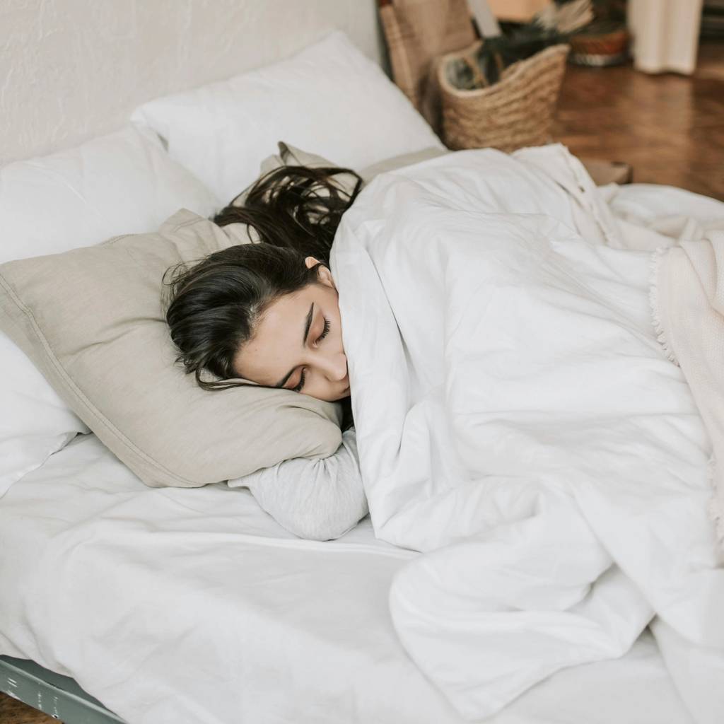 Woman sleeping on her side in a white bed under a white duvet.