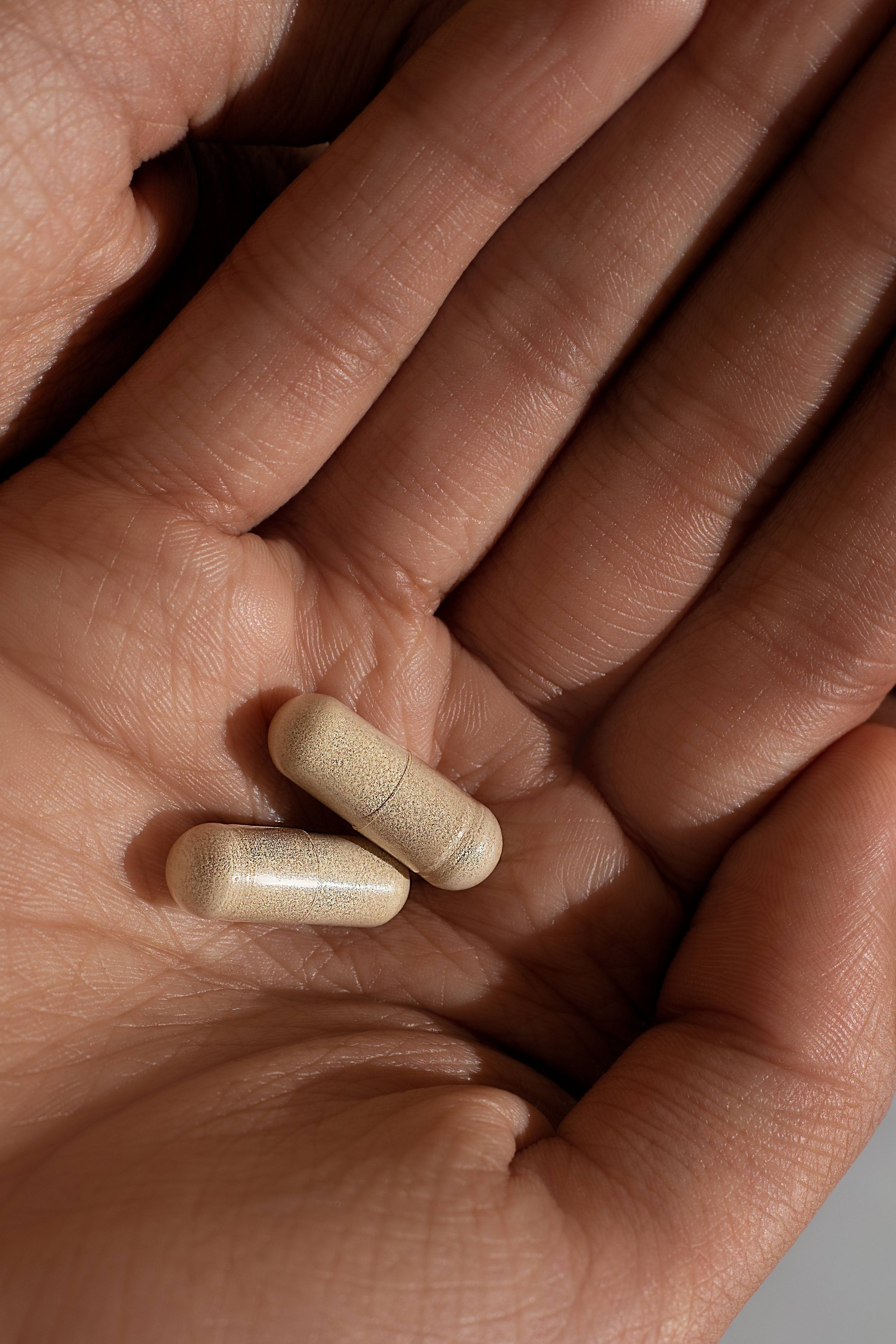 Two beige capsules resting in an open hand.