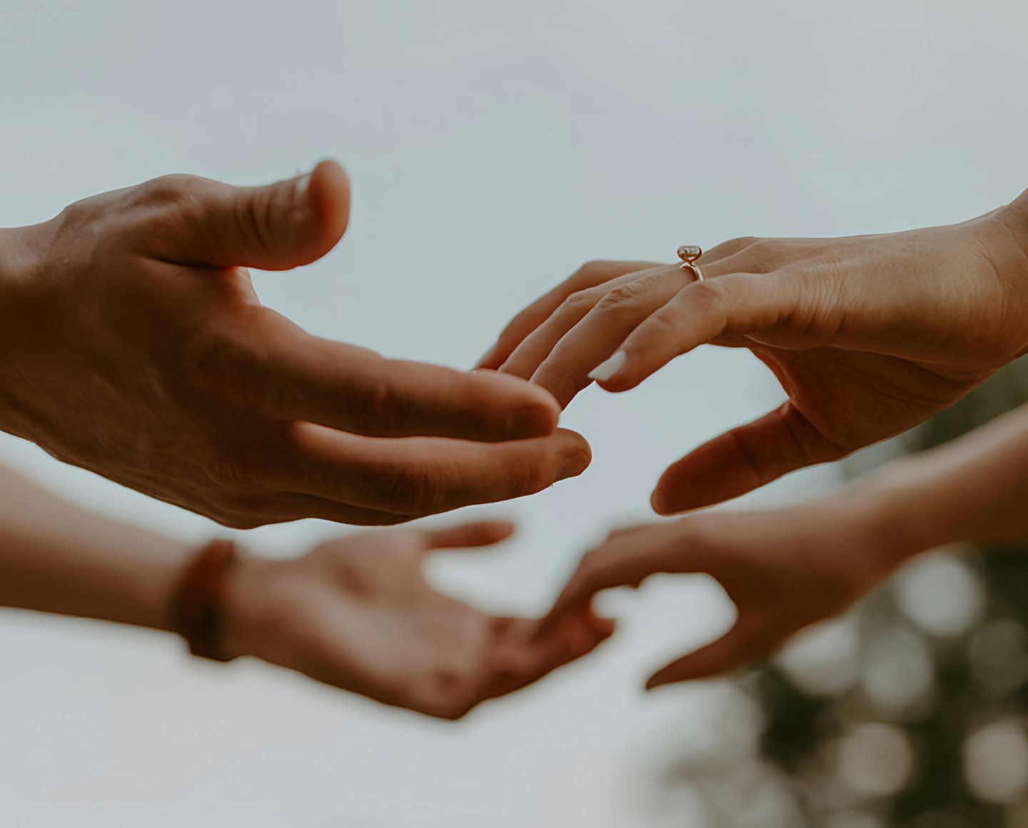Several hands reach toward one another, with a ring on one hand.