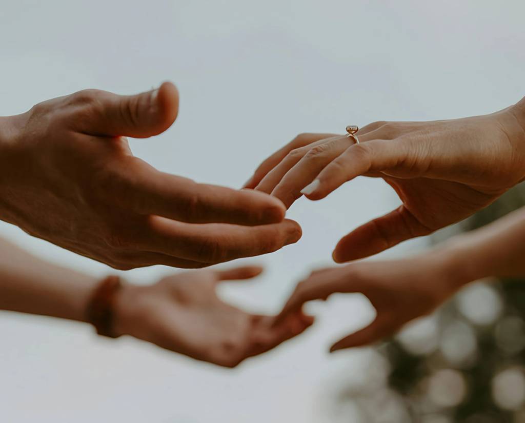 Several hands reach toward one another, with a ring on one hand.