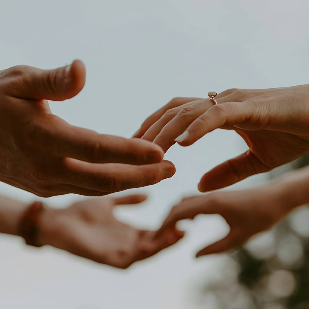 Several hands reach toward one another, with a ring on one hand.