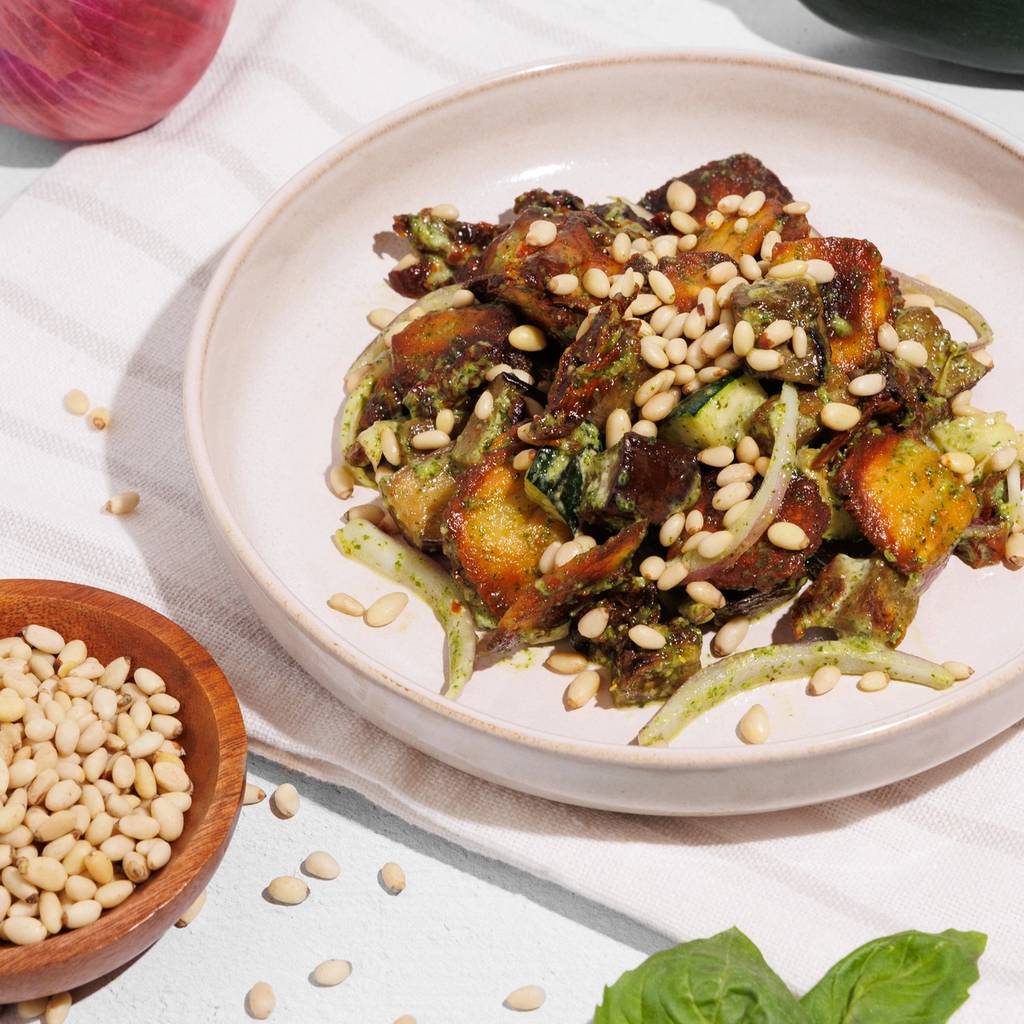 Plate of crispy gnocchi salad with pesto, zucchini, onion, and pine nuts, surrounded by fresh ingredients.