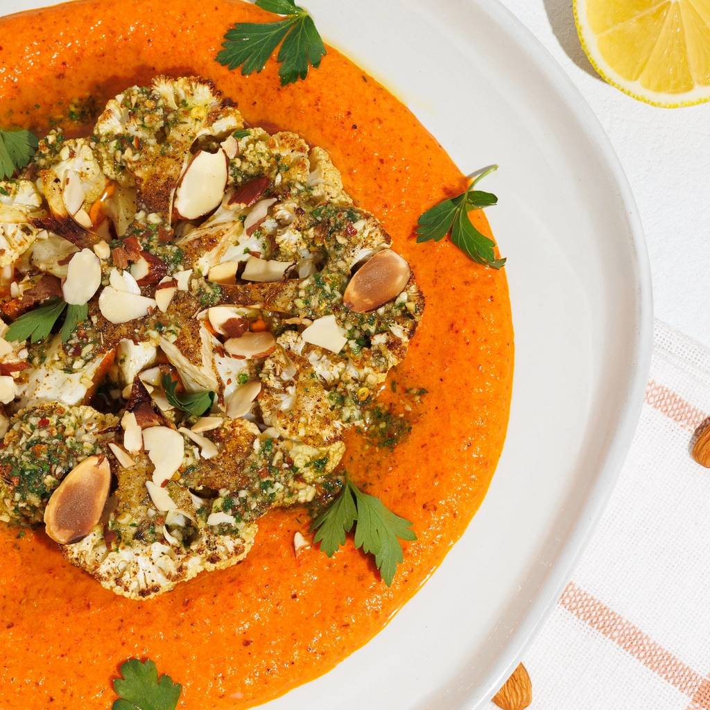 Roasted cauliflower steak with orange sauce, almonds, parsley, lemon, and a bowl of almonds.
