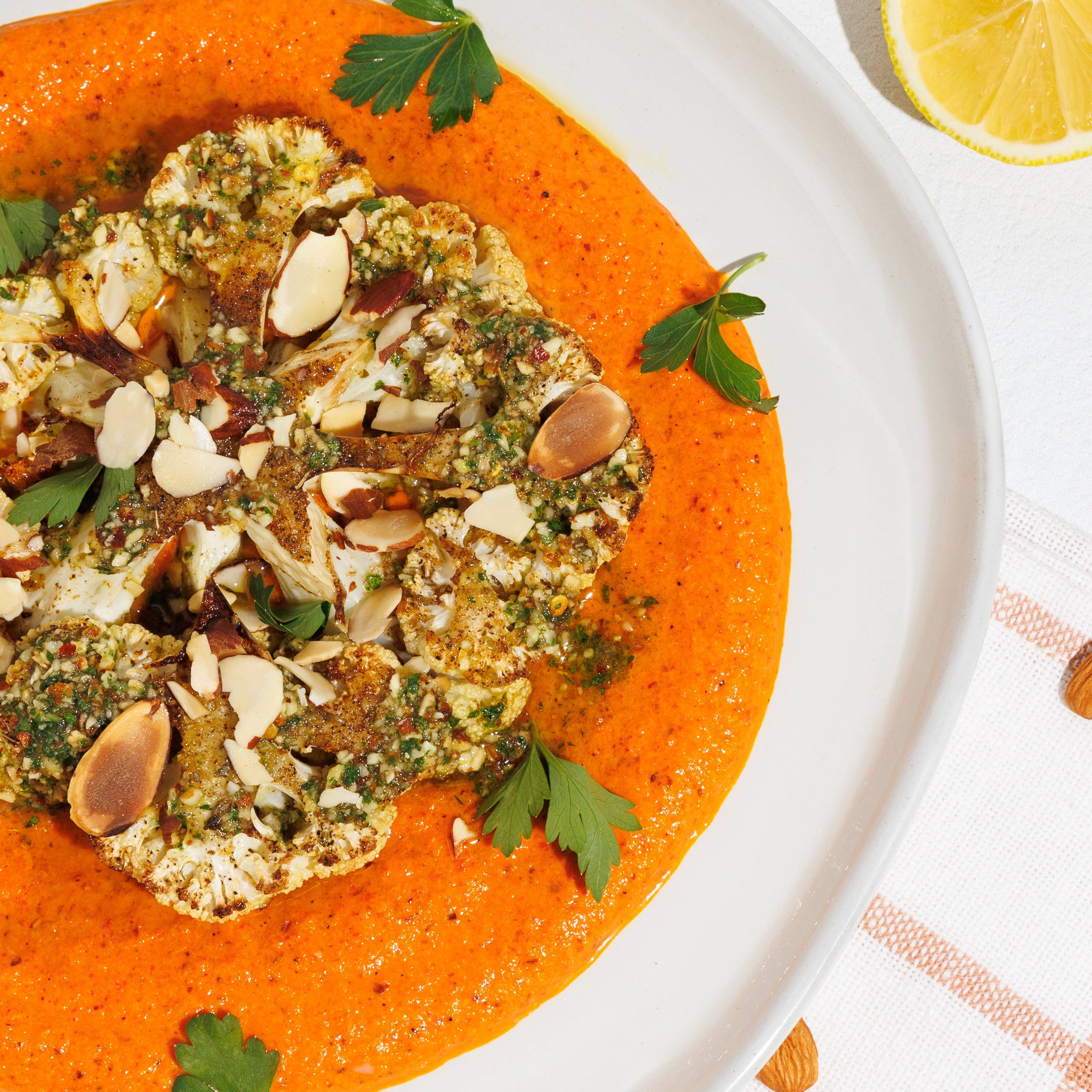 Roasted cauliflower steak with orange sauce, almonds, parsley, lemon, and a bowl of almonds.