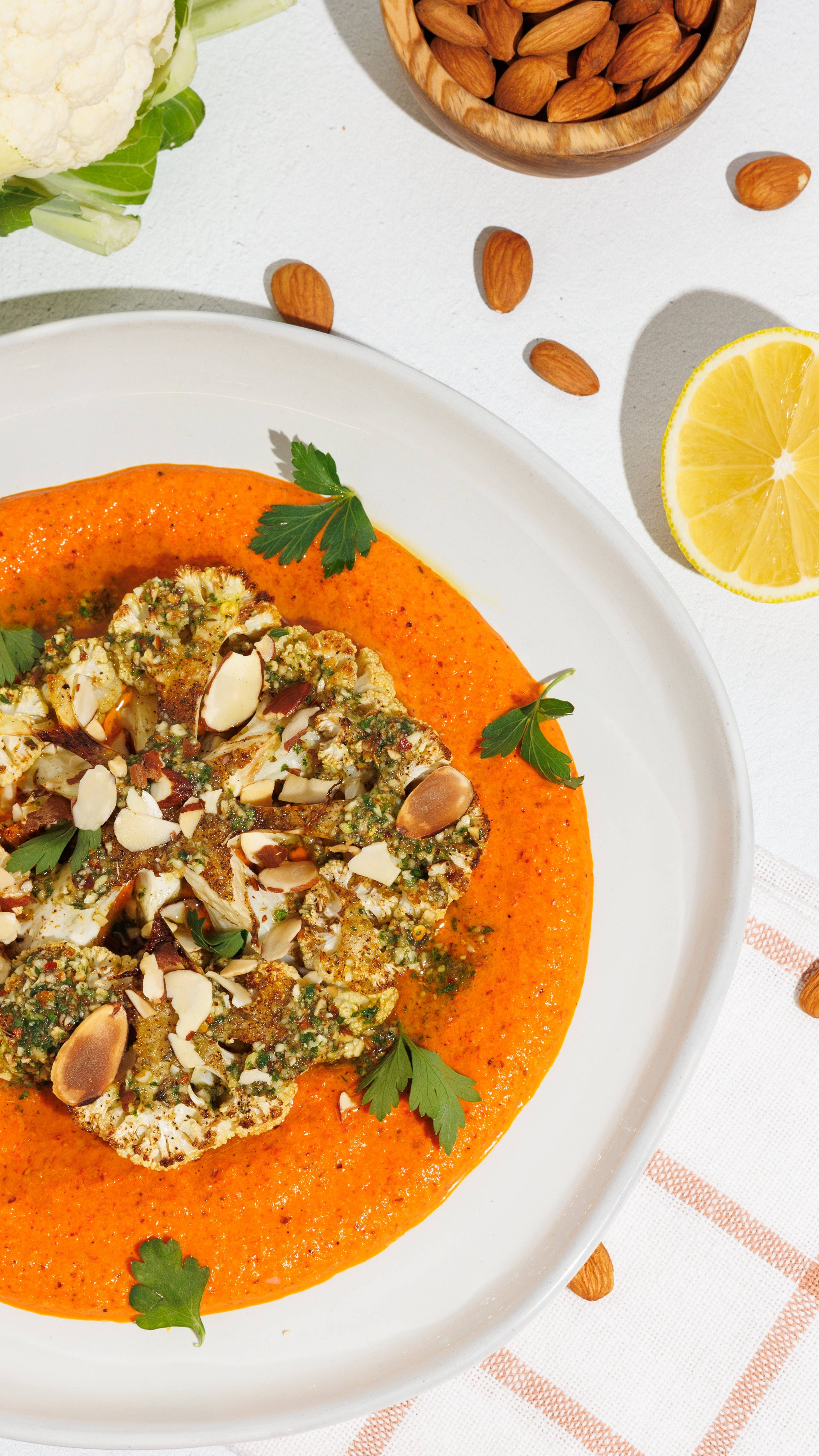 Roasted cauliflower steak with orange sauce, almonds, parsley, lemon, and a bowl of almonds.