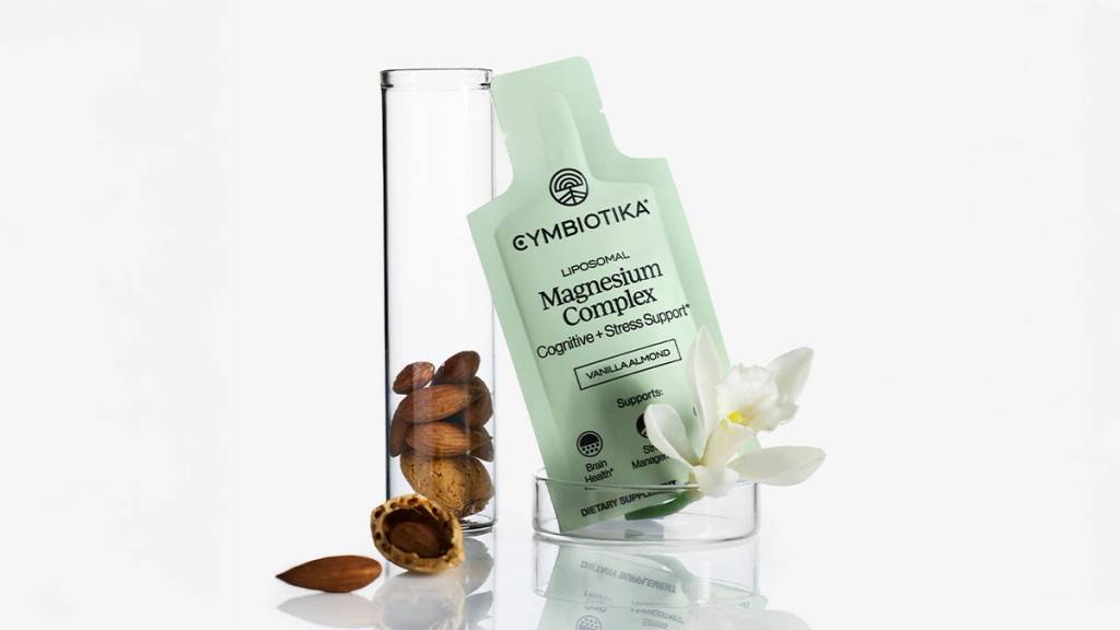 Cymbiotika Liposomal Magnesium Complex packet beside a glass cylinder, almonds, and a white flower.