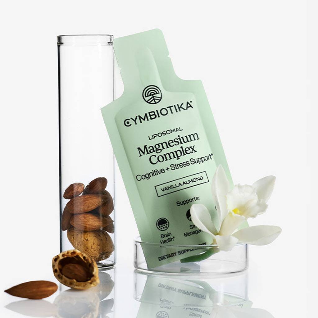 Cymbiotika Liposomal Magnesium Complex packet beside a glass cylinder, almonds, and a white flower.