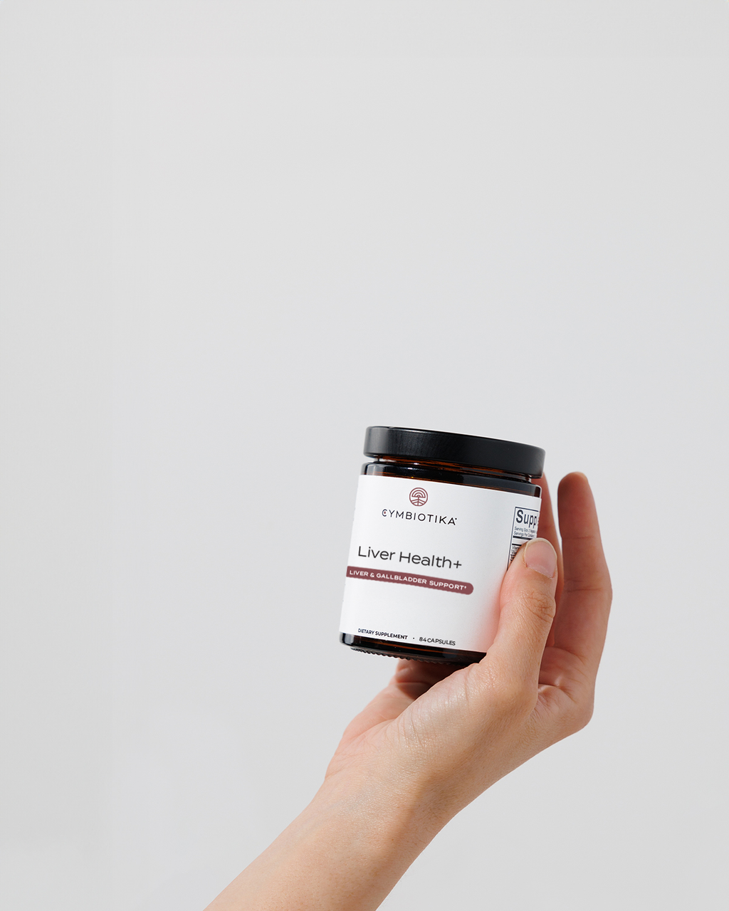 A hand holds a jar labeled Cymbiotika Liver Health+.