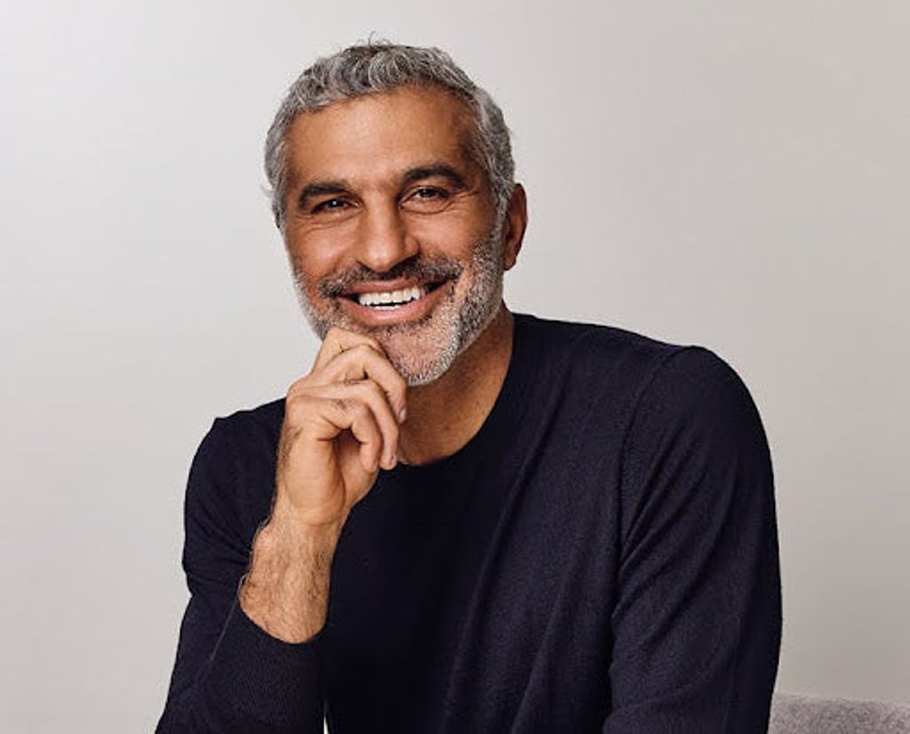 Smiling gray-haired man in a dark sweater resting his hand beneath his chin.