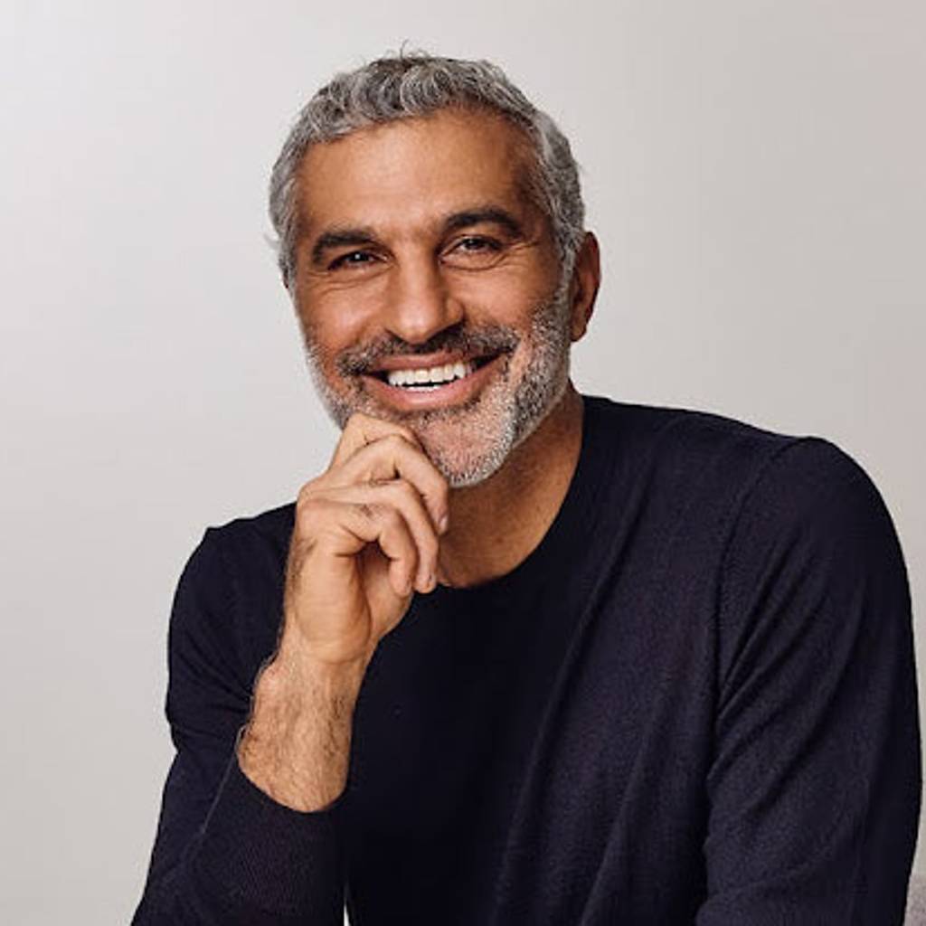 Smiling gray-haired man in a dark sweater resting his hand beneath his chin.