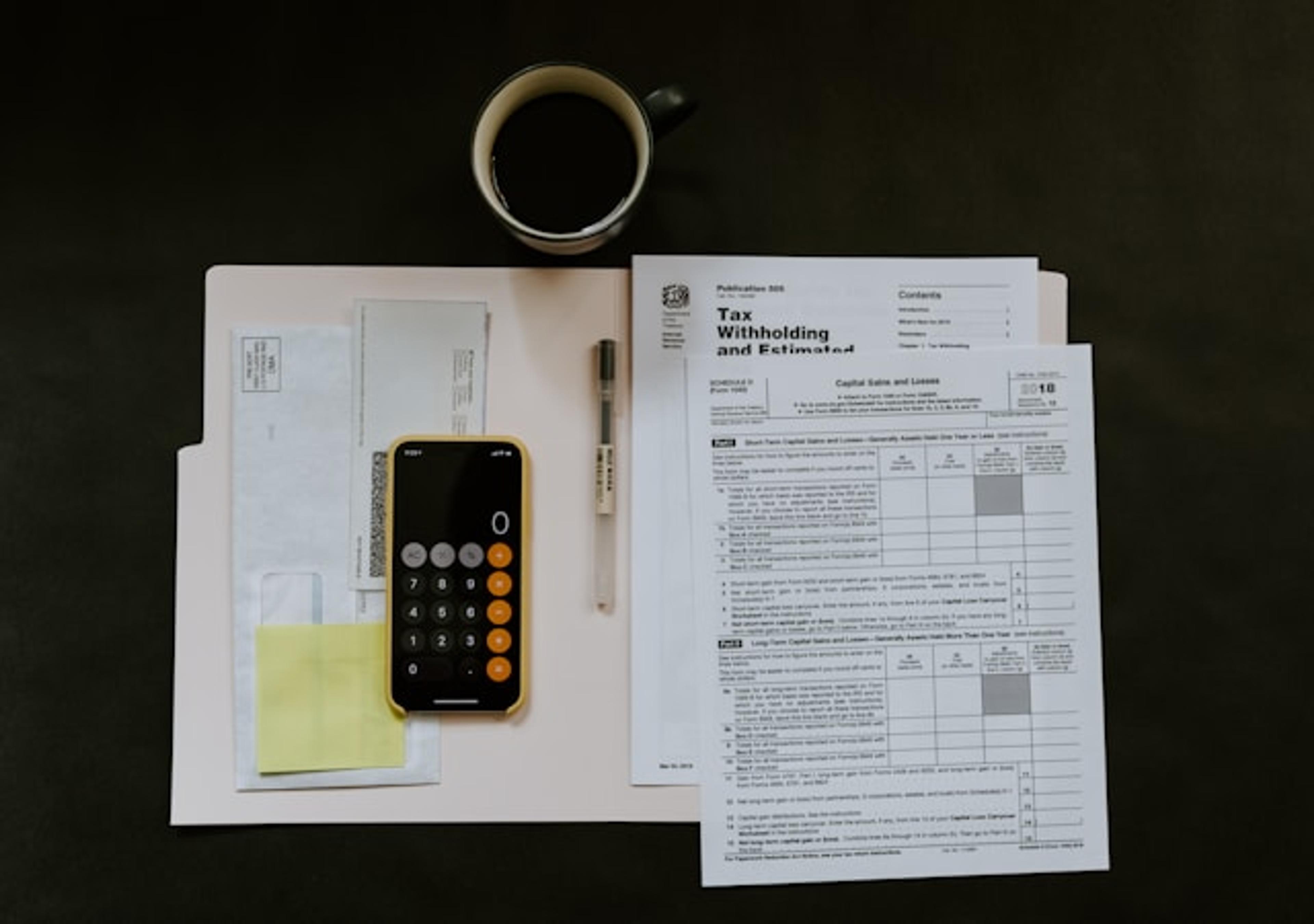 A table with coffee, a smartphone with calculator view open, and some papers featuring tax filing documents.