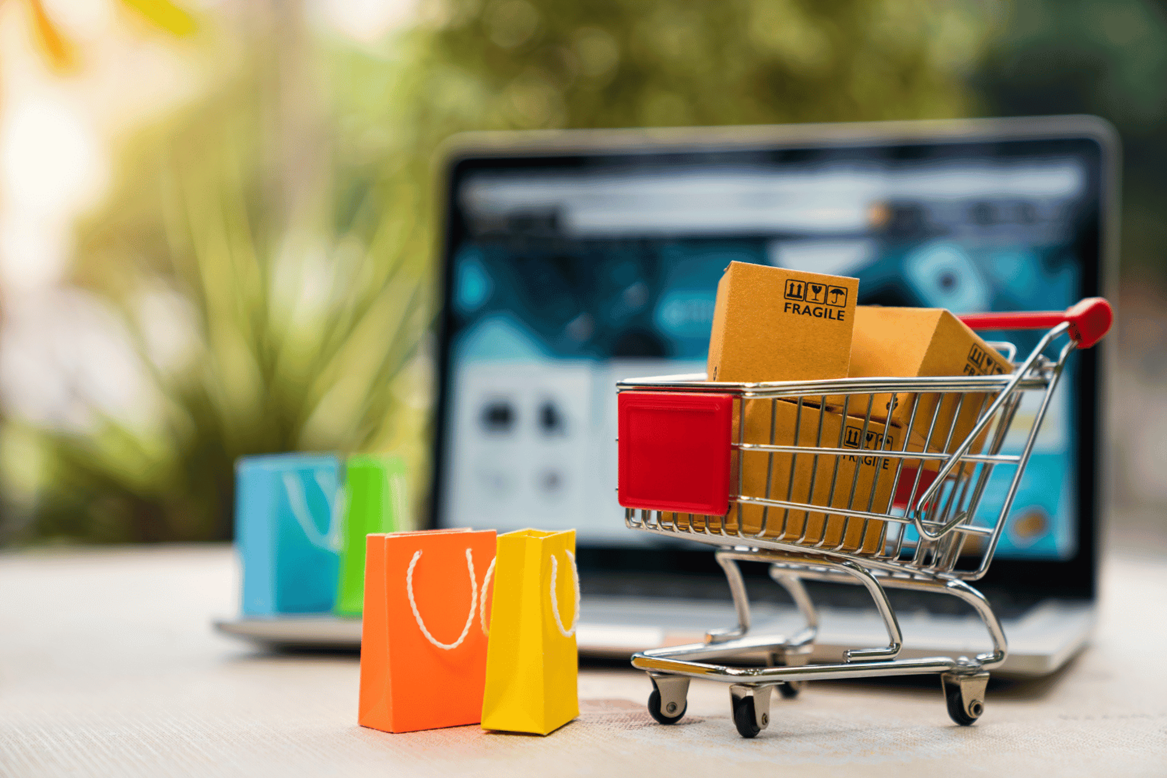 Miniature shopping cart and shopping bags with full of items in front of a laptop