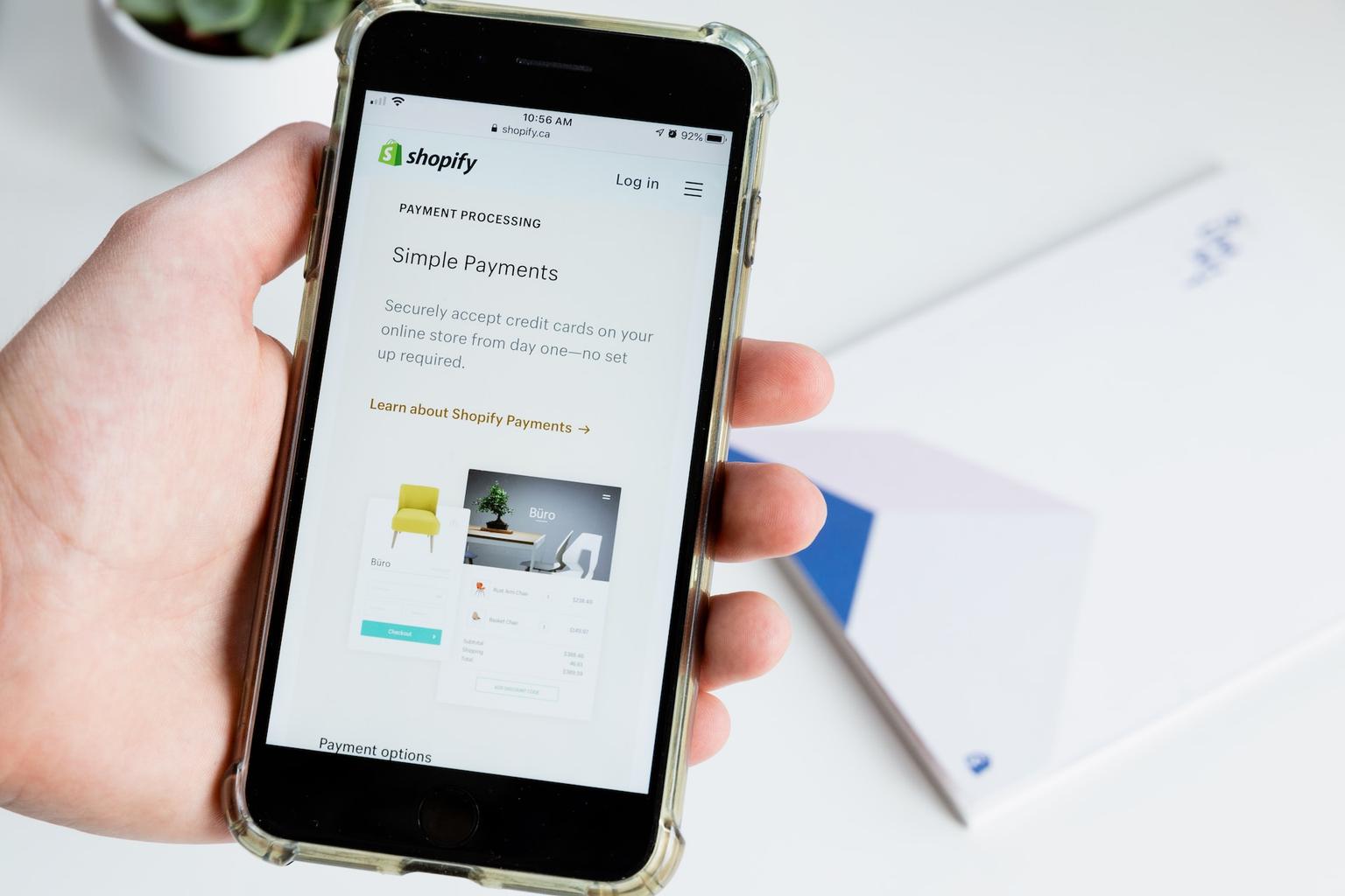 Hand holding a phone featuring Shopify Payments in the browser.