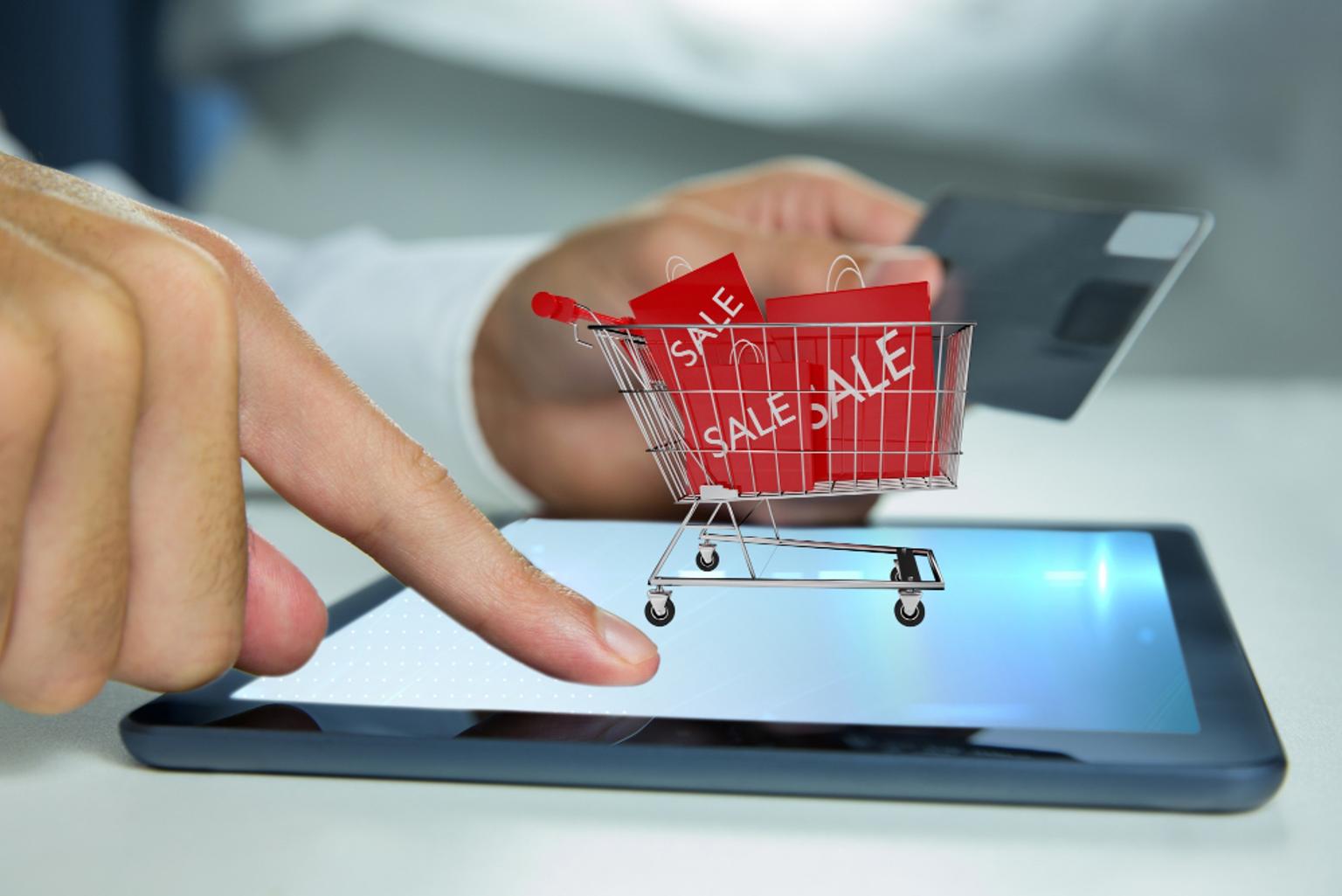 A person touching a tablet to buy eCommerce products while presenting a shopping cart full of sale bags