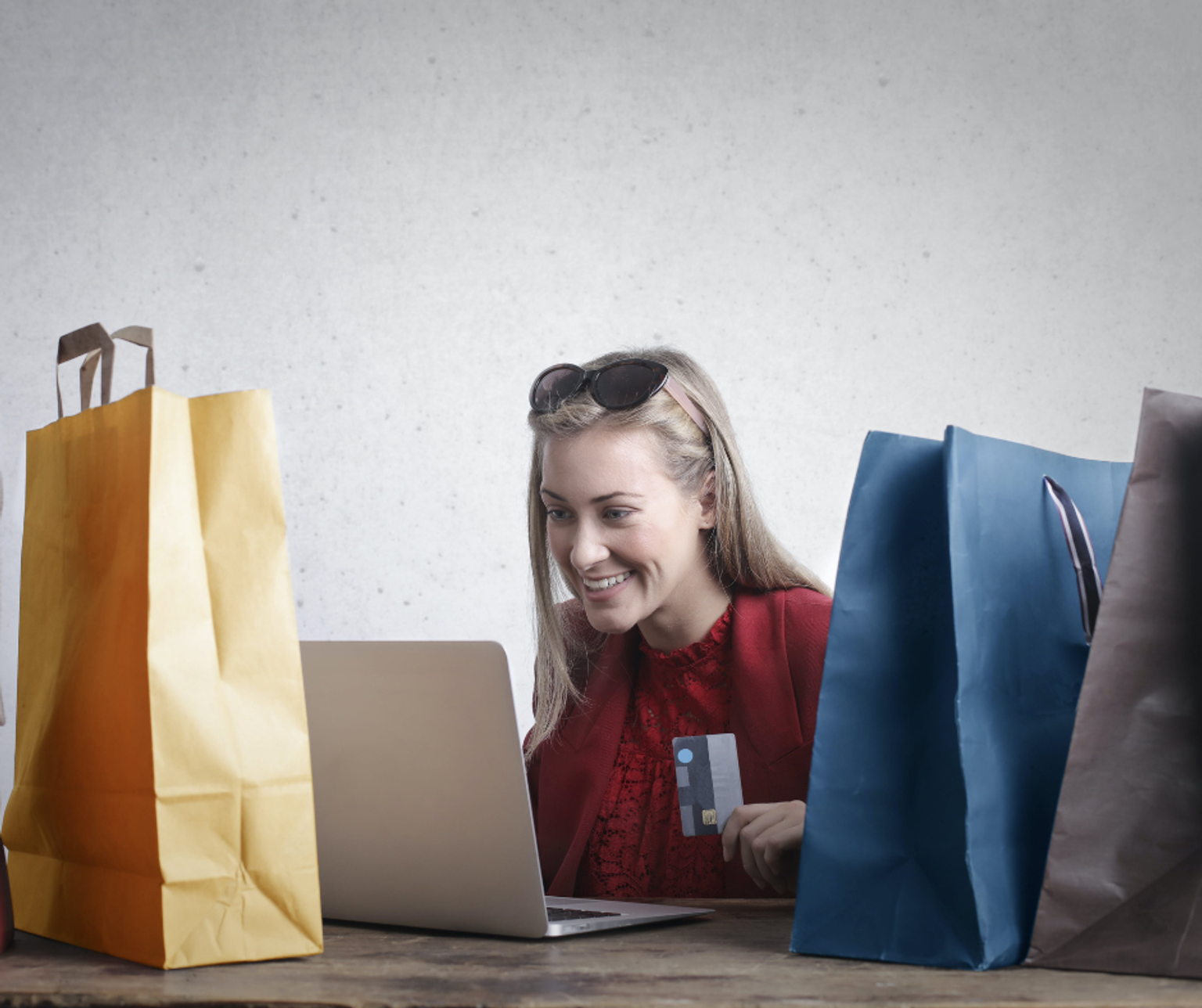 Women purchasing goods online with a credit card surrounded by shopping bags.