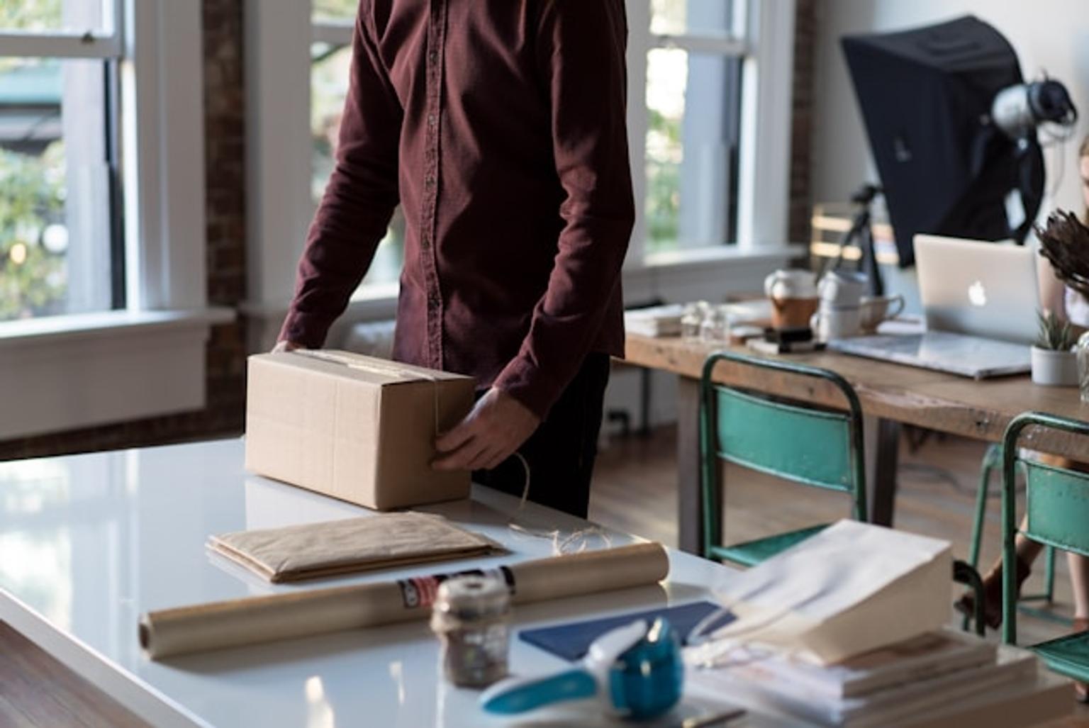 Person packaging unique goods for online selling in a studio with laptop and photography equipment