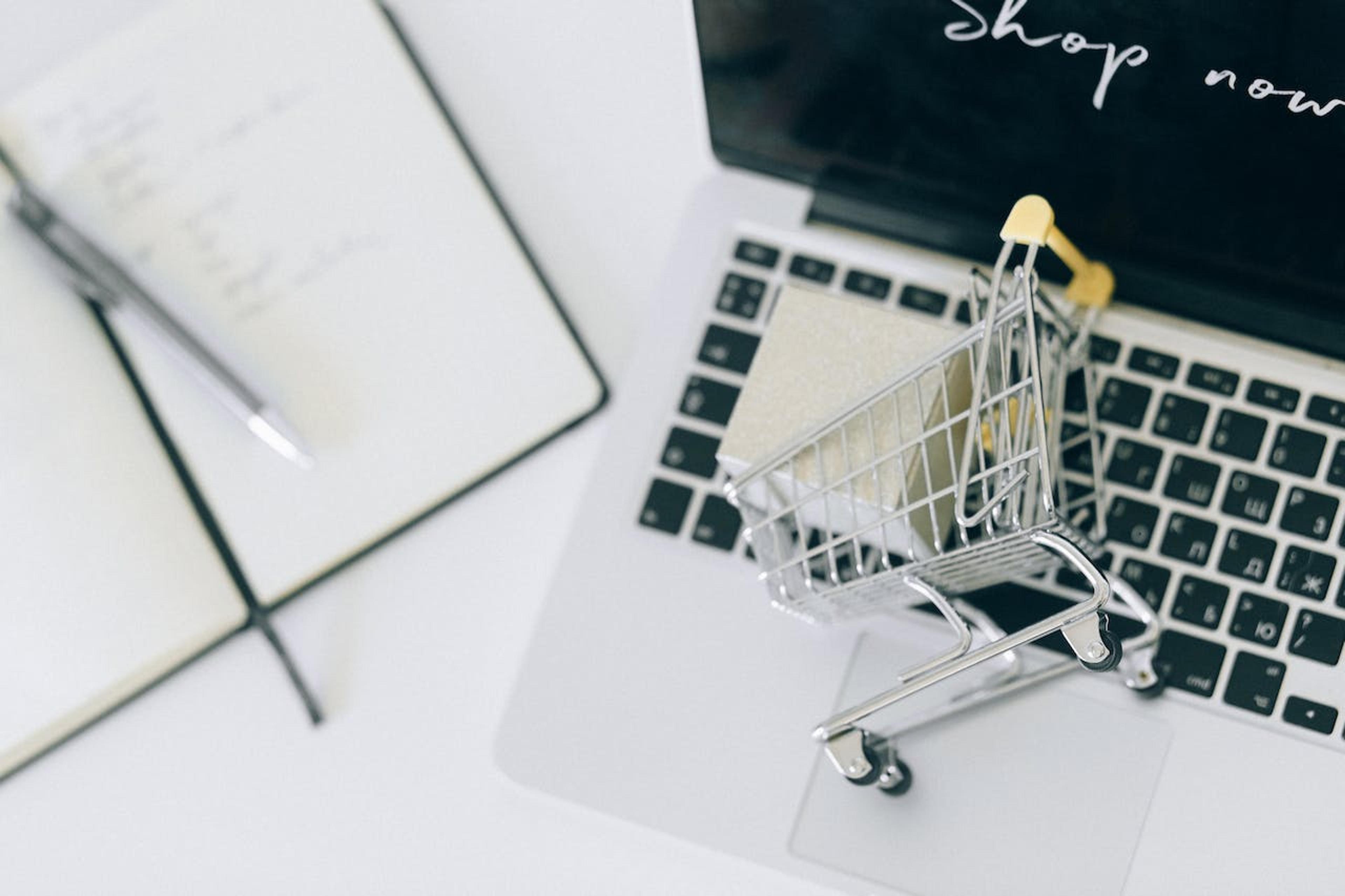 A shopping cart laying on a laptop illustrating online shopping.
