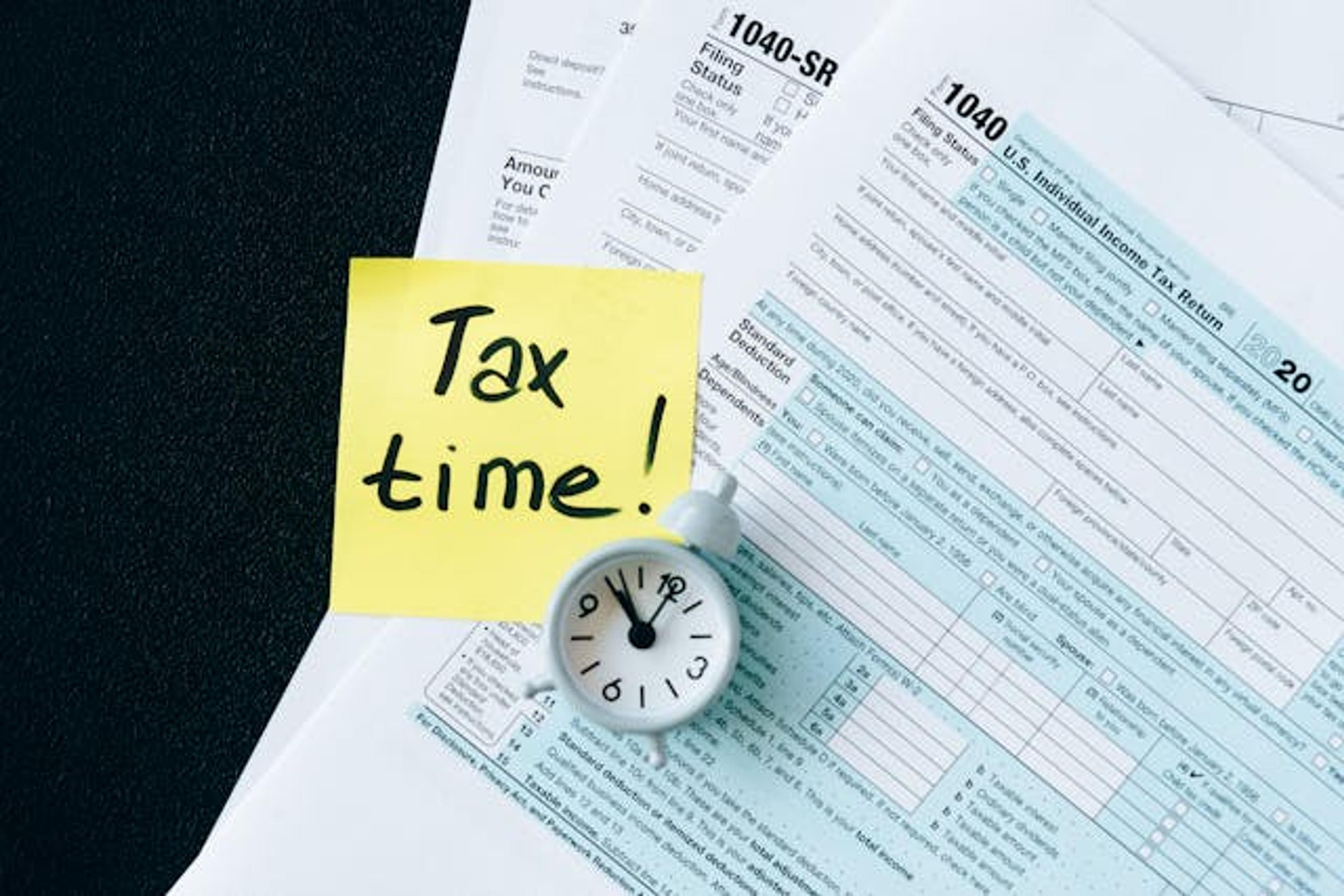 Image of a desktop featuring tax filing forms, a clock and a sticky note with the text tax time.