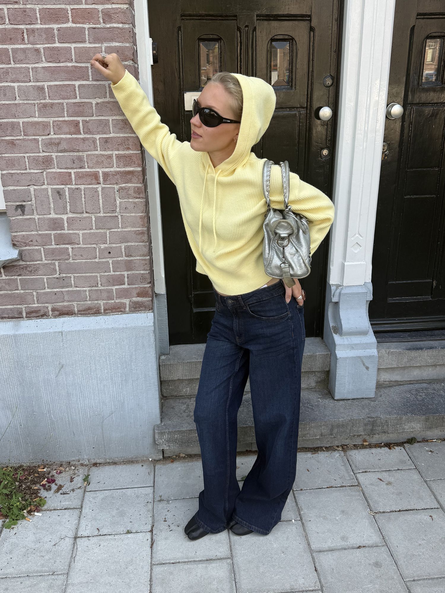 Woman wearing a light yellow hooded sweater, dark wide-leg jeans and black shoes.