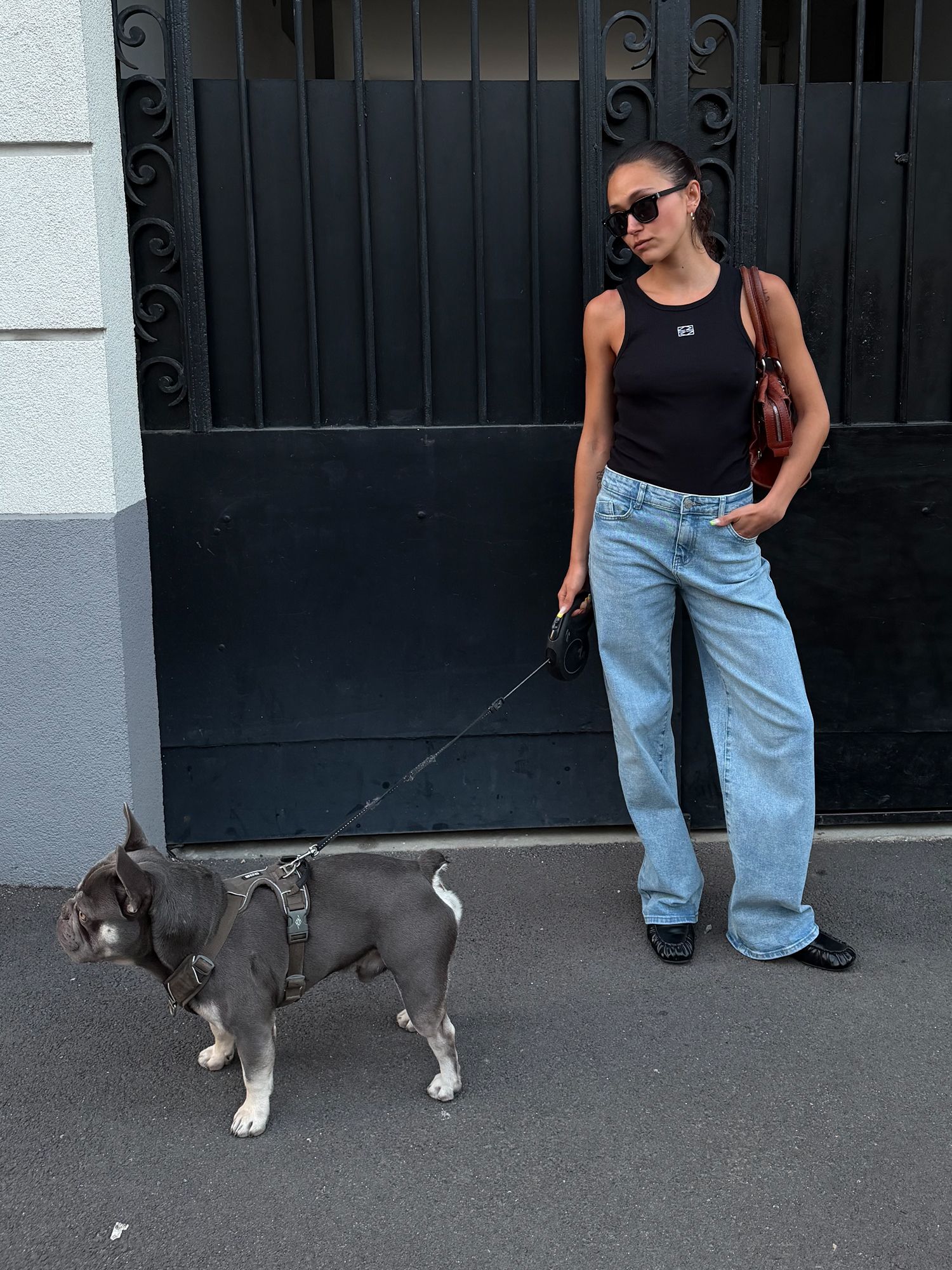 Woman wearing a black tank top, light blue wide-leg jeans and black shoes.
