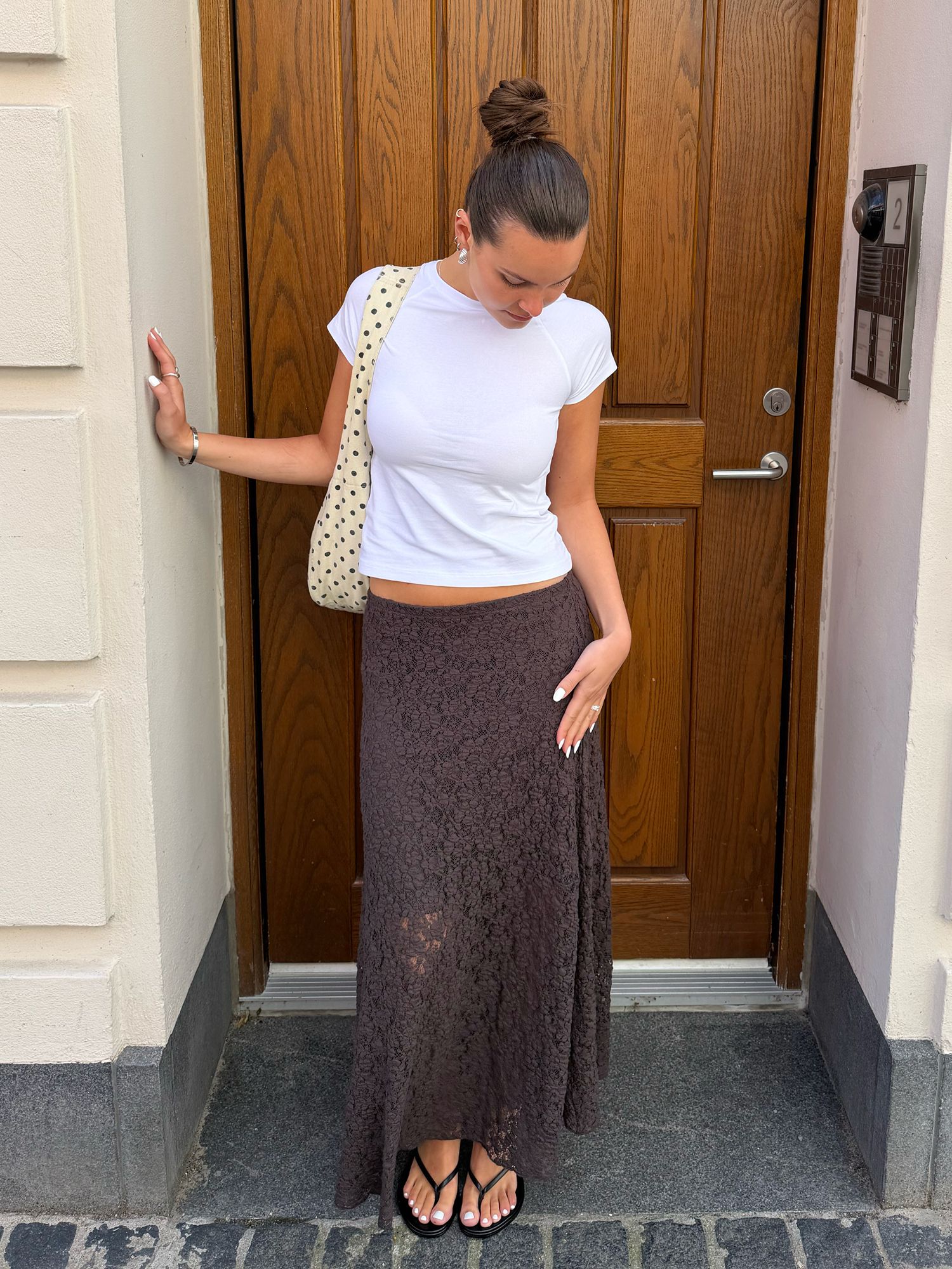 Woman wearing a white T-shirt, long brown lace skirt and black sandals