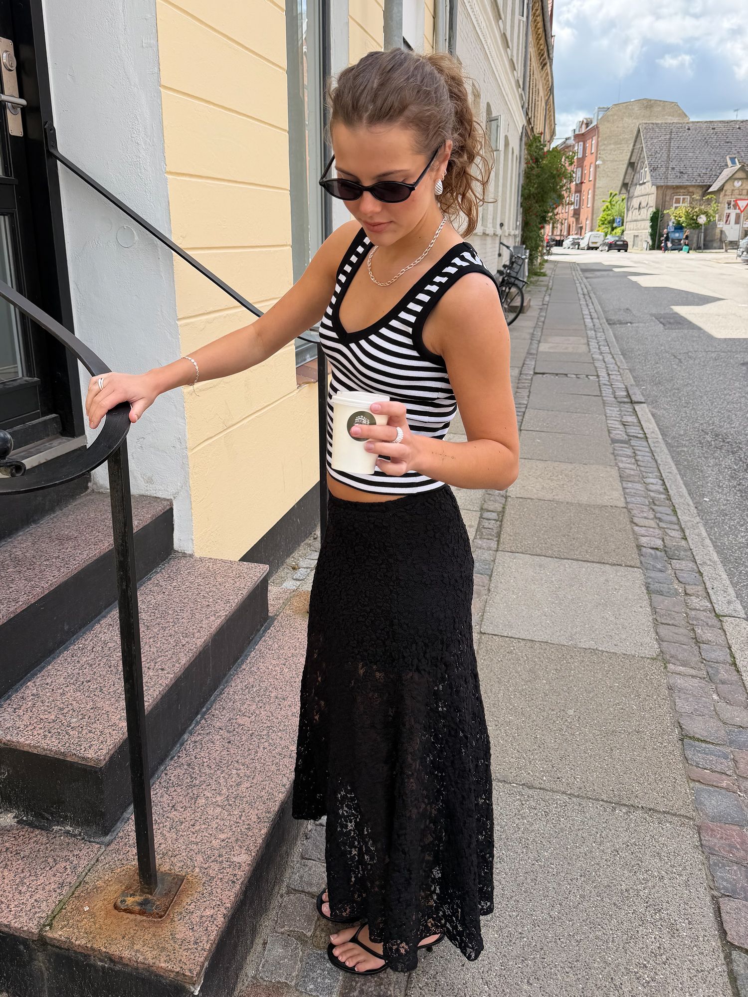 Woman wearing a black and white striped tank top, long black lace skirt and black sandals.