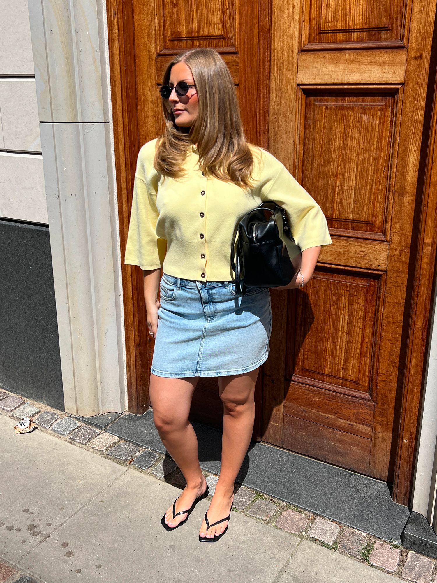 Woman wearing a light yellow cardigan, denim mini skirt and black sandals.