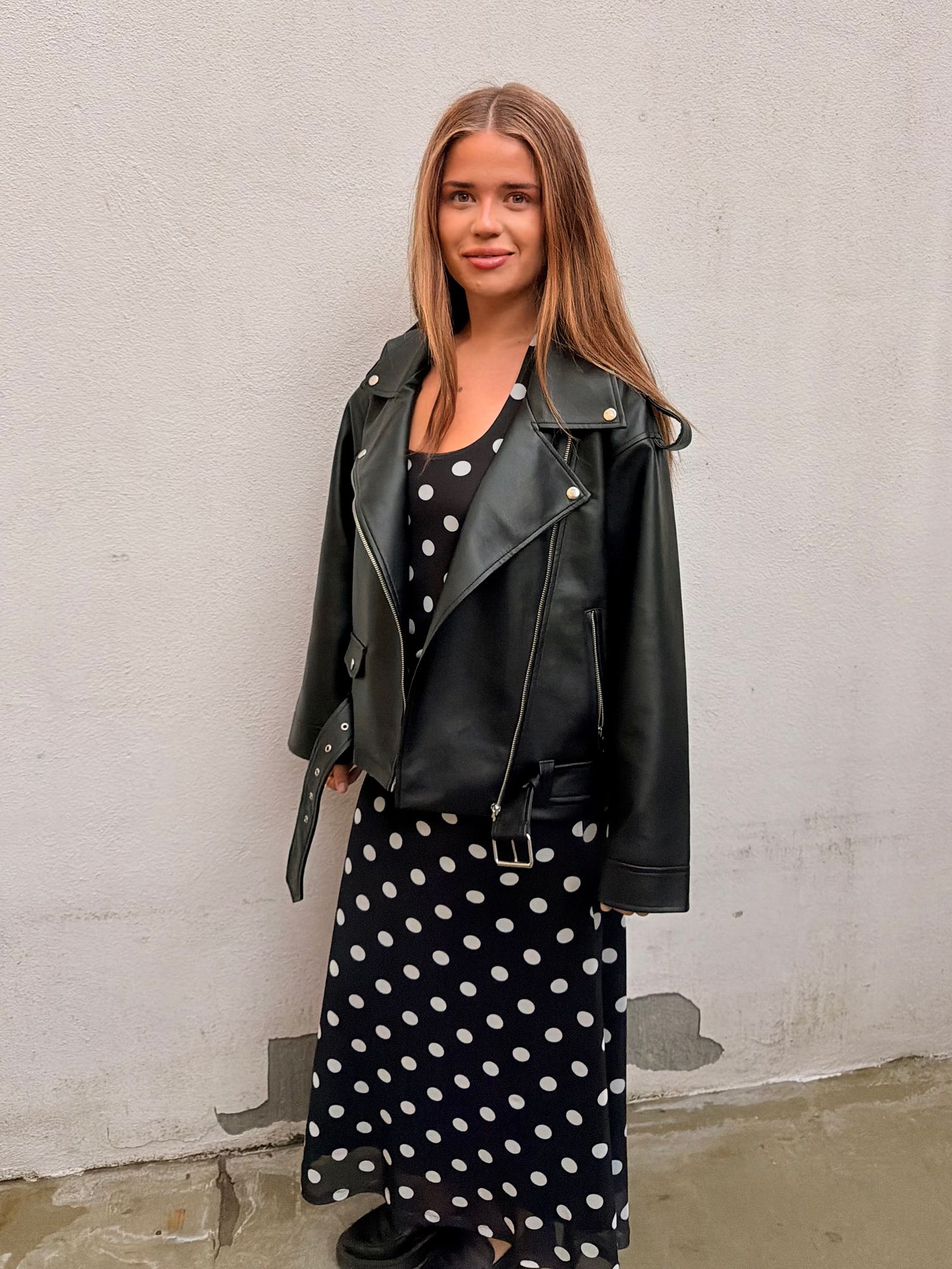 Woman wearing a black leather jacket, black and white polka dot top and matching skirt.