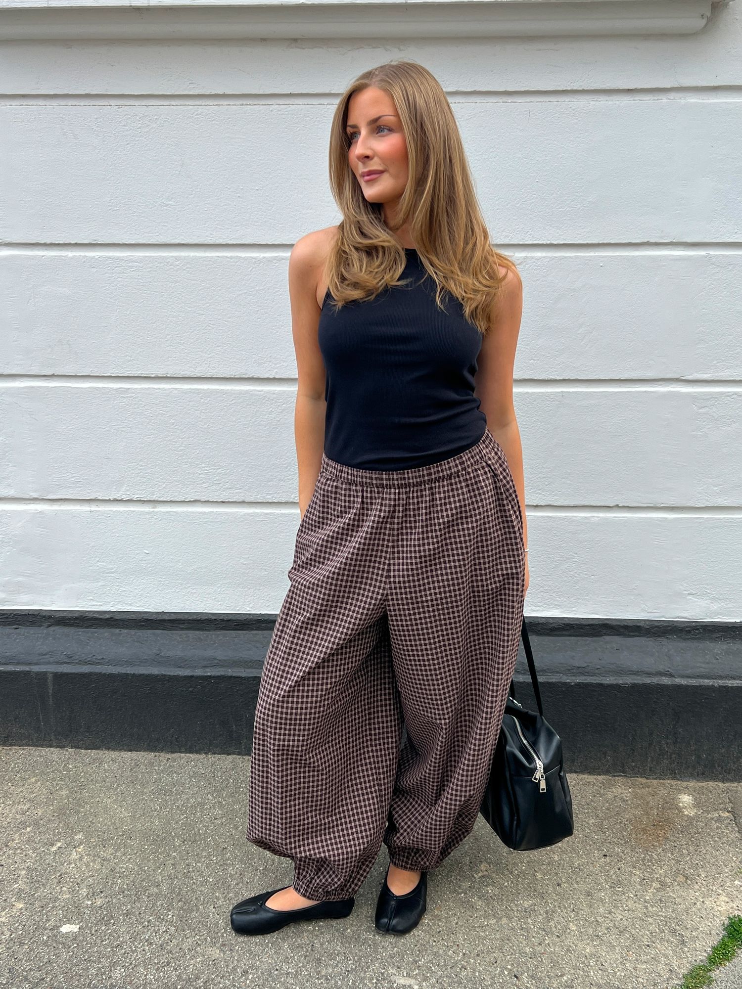 oman wearing a black sleeveless top, brown check trousers and black ballet flats.