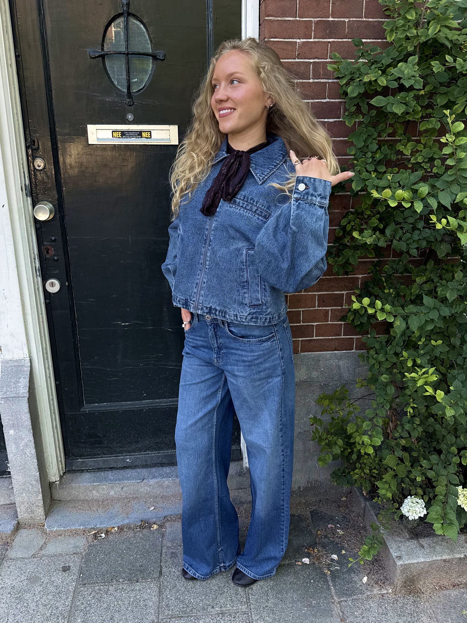 Woman wearing a blue denim jacket with a dark collar and matching wide-leg jeans.