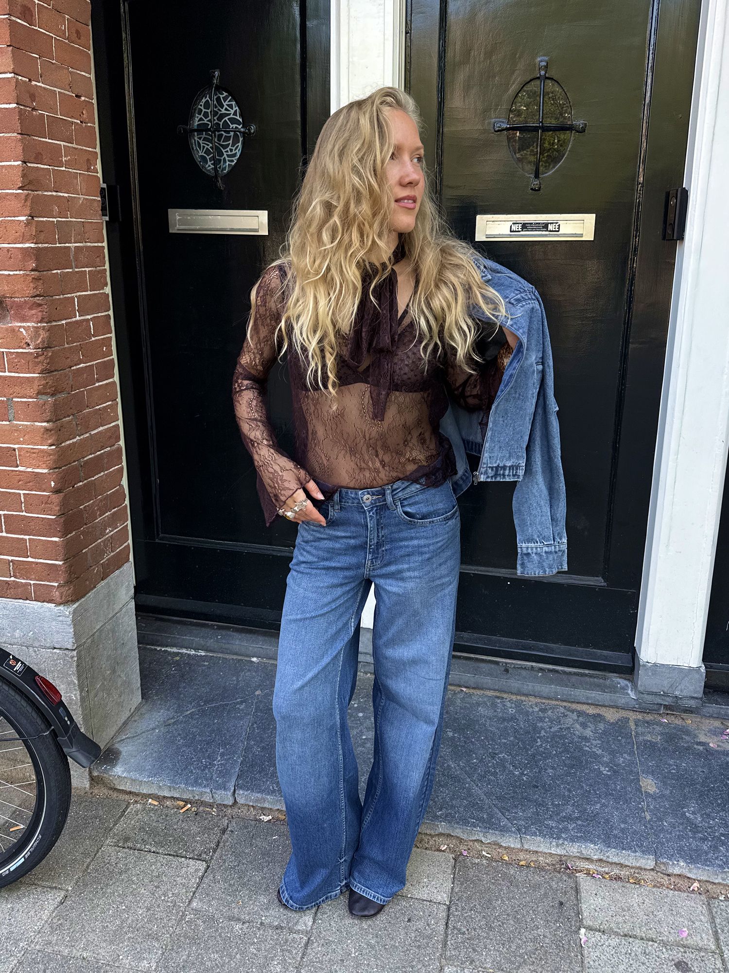 Woman wearing a brown lace top, light blue wide-leg jeans and a denim jacket.