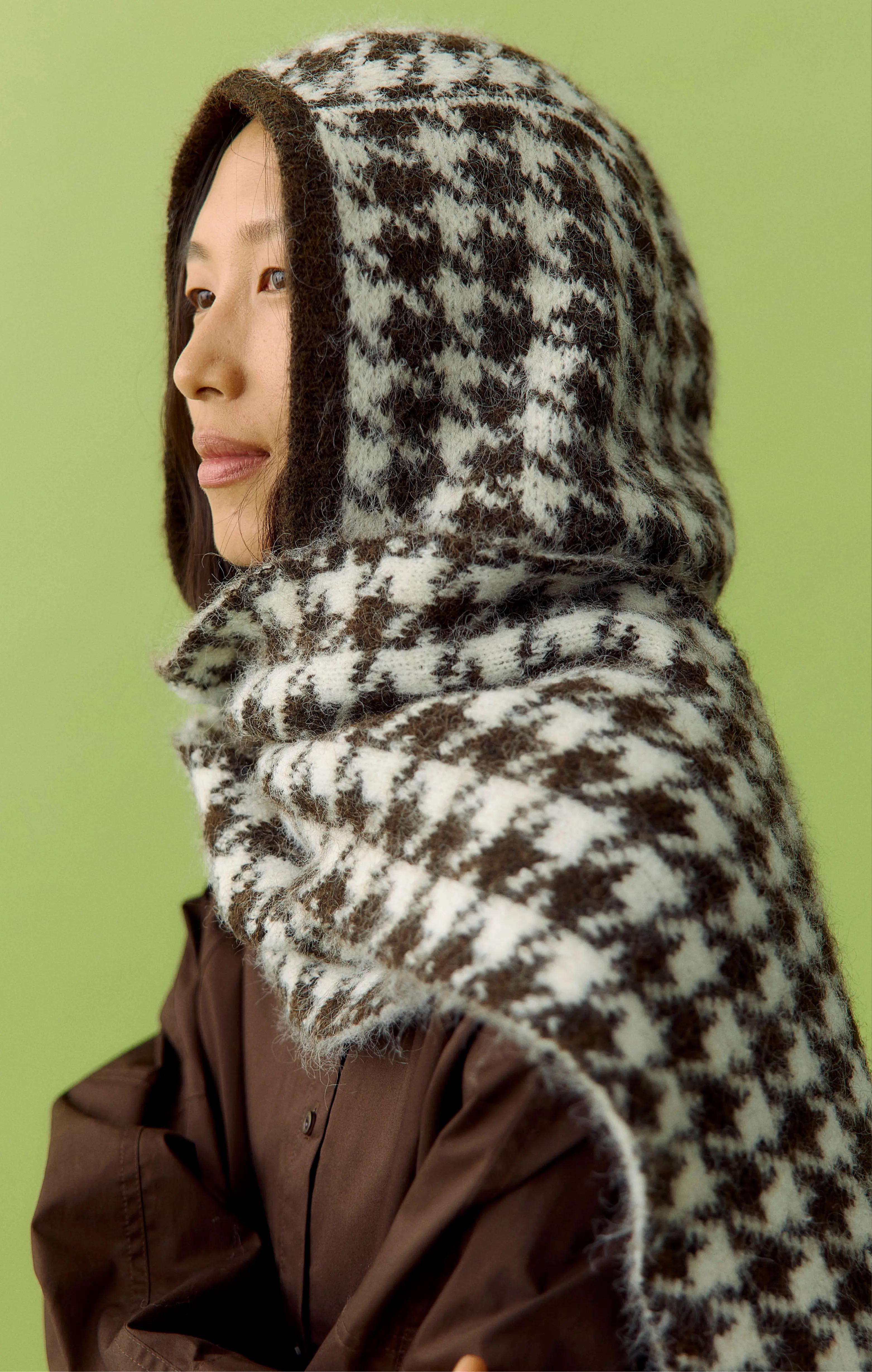 Profile of an Asian woman in a brown-and-white houndstooth hood and scarf on green.