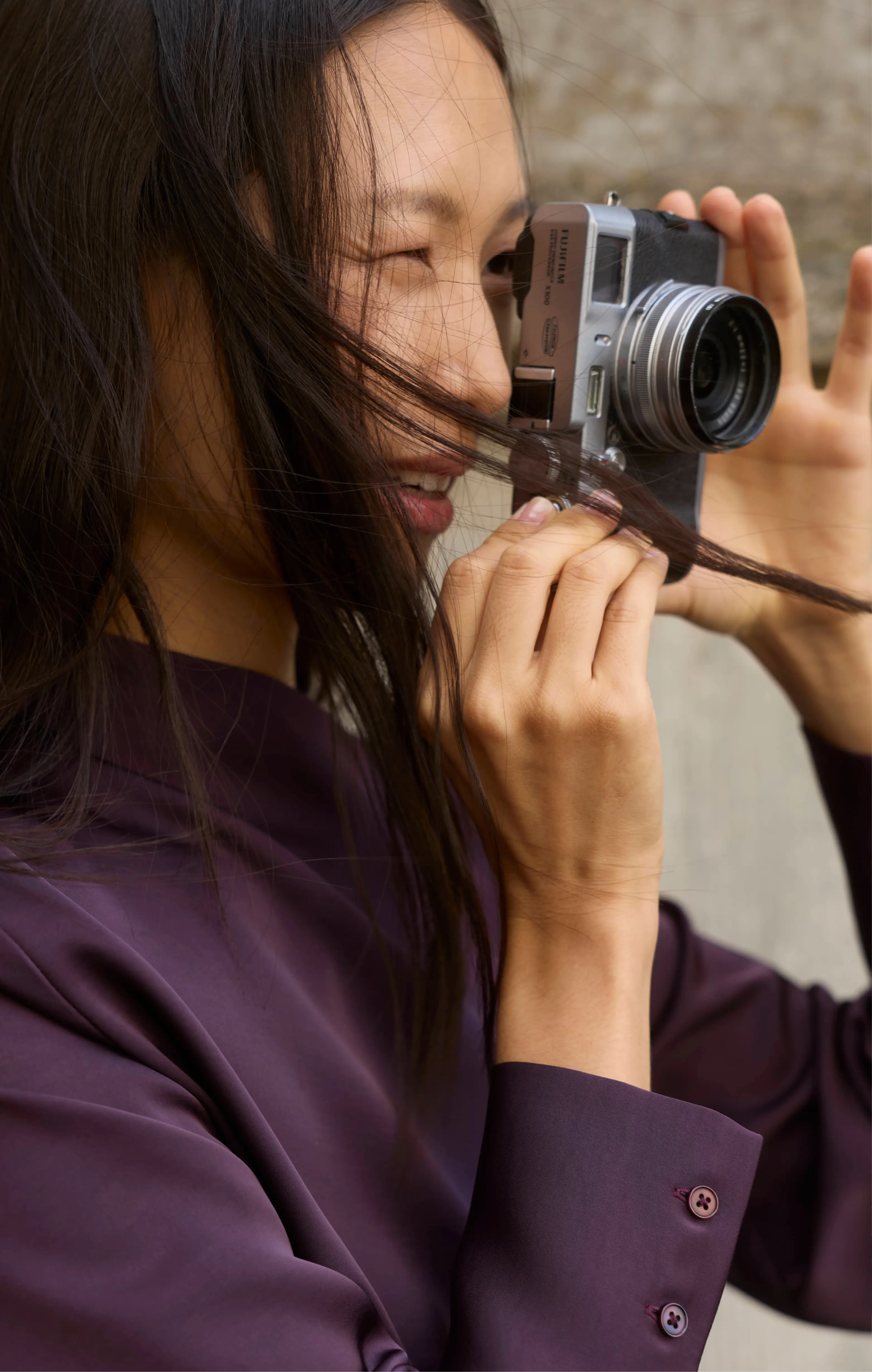 Smiling woman in a purple blouse holding a Fujifilm camera to the viewfinder