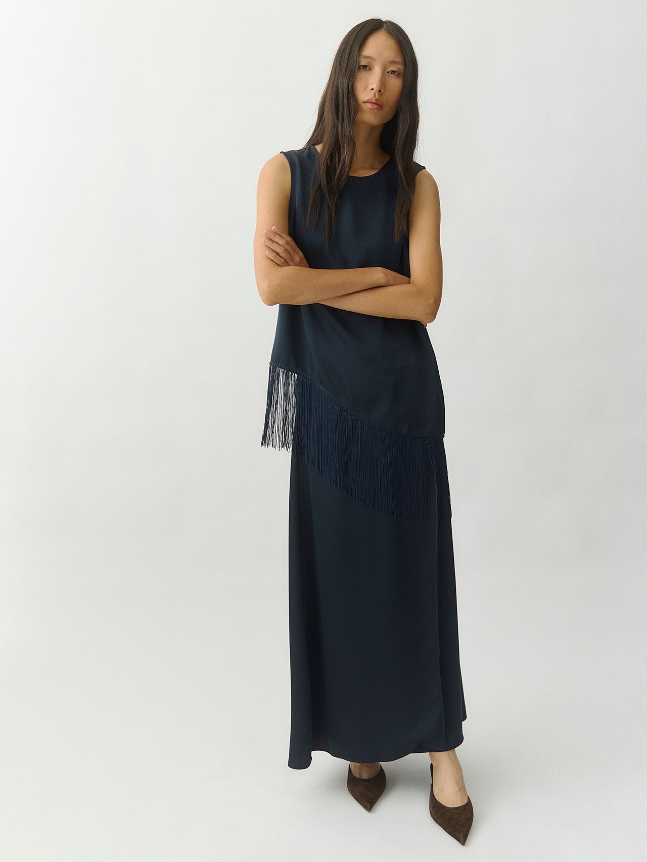 Woman in a navy blue fringed two-piece set and pointed-toe heels on a white background