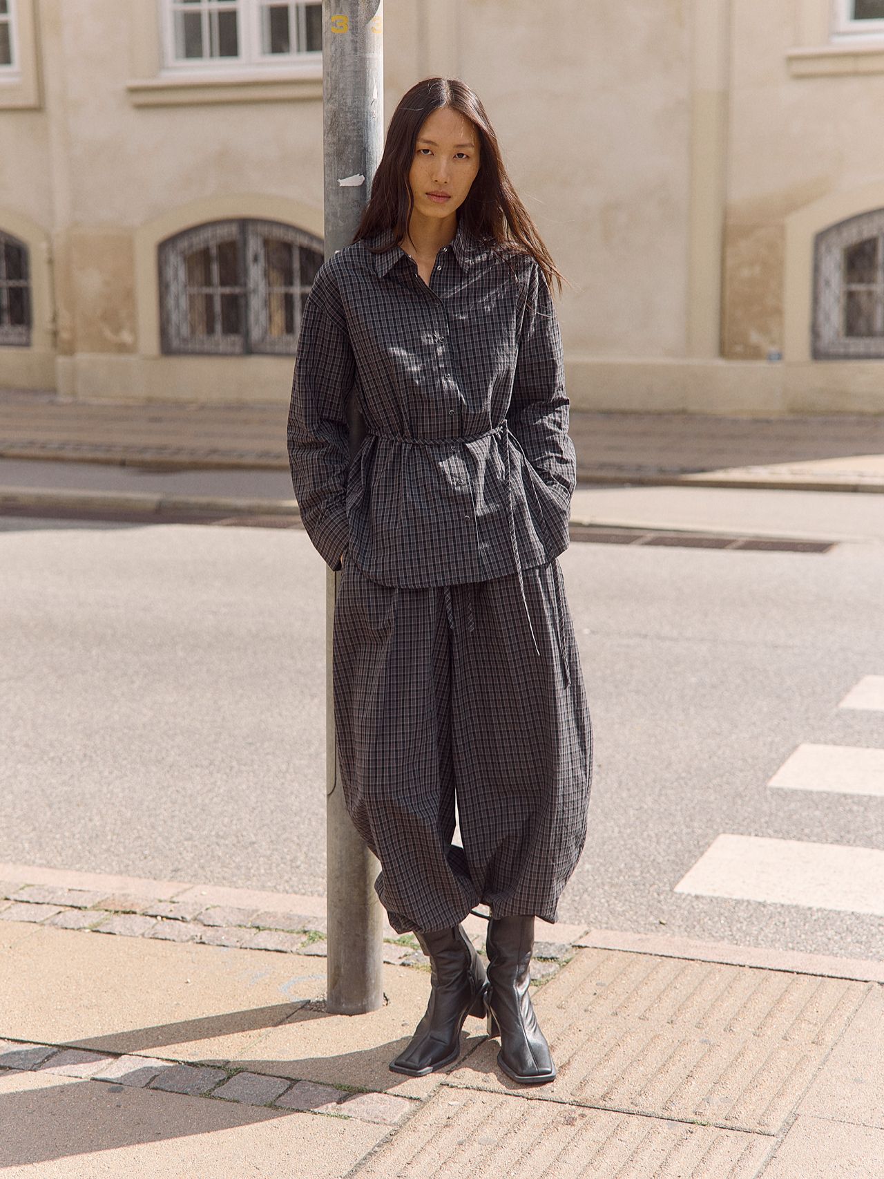 Woman in oversized plaid shirt and pants with black boots on a city street.