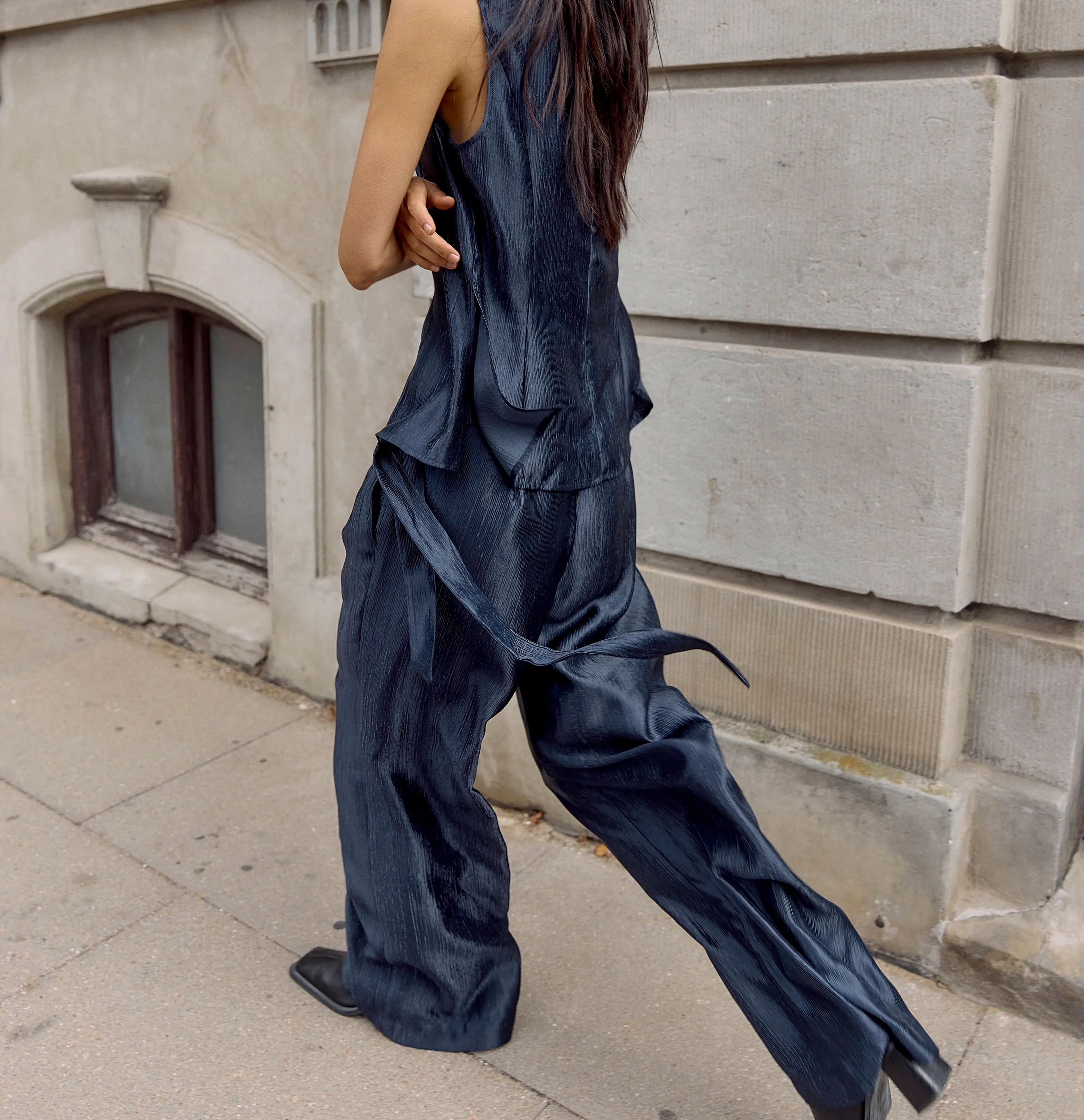 Woman in a navy sleeveless top and flowy wide-leg pants walking on an urban sidewalk.