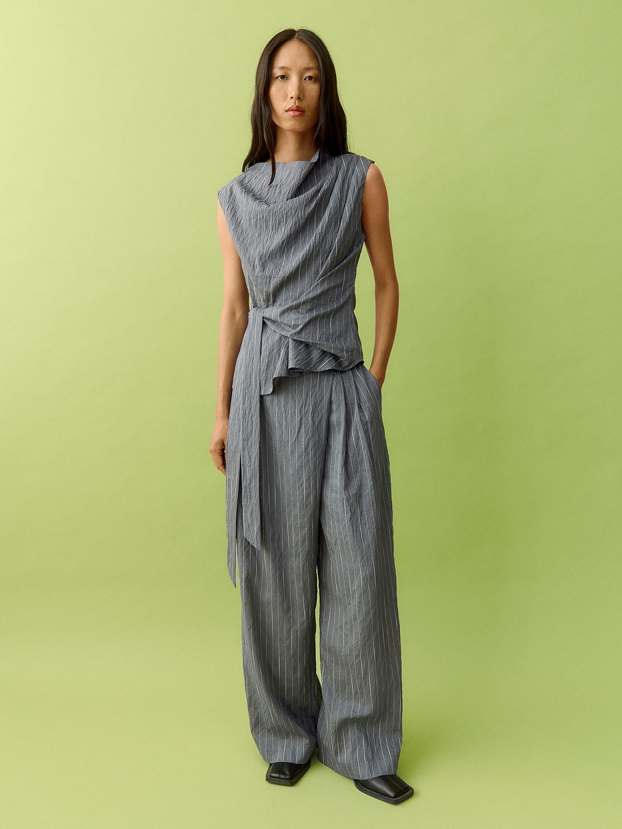 Woman in grey pinstripe co-ord and black flats standing against a lime green background