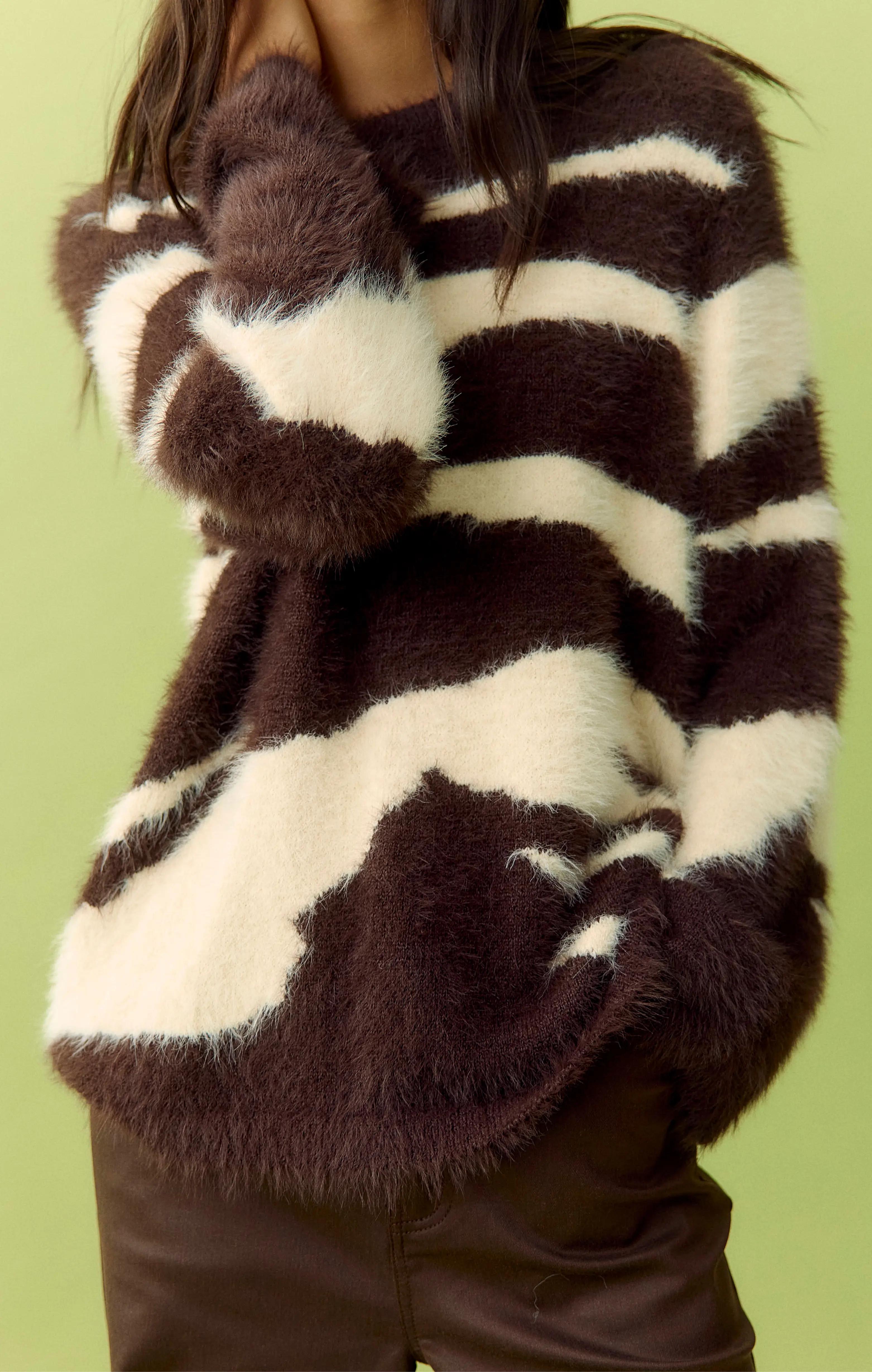 Fuzzy brown and cream cow-print sweater with long sleeves on a green background