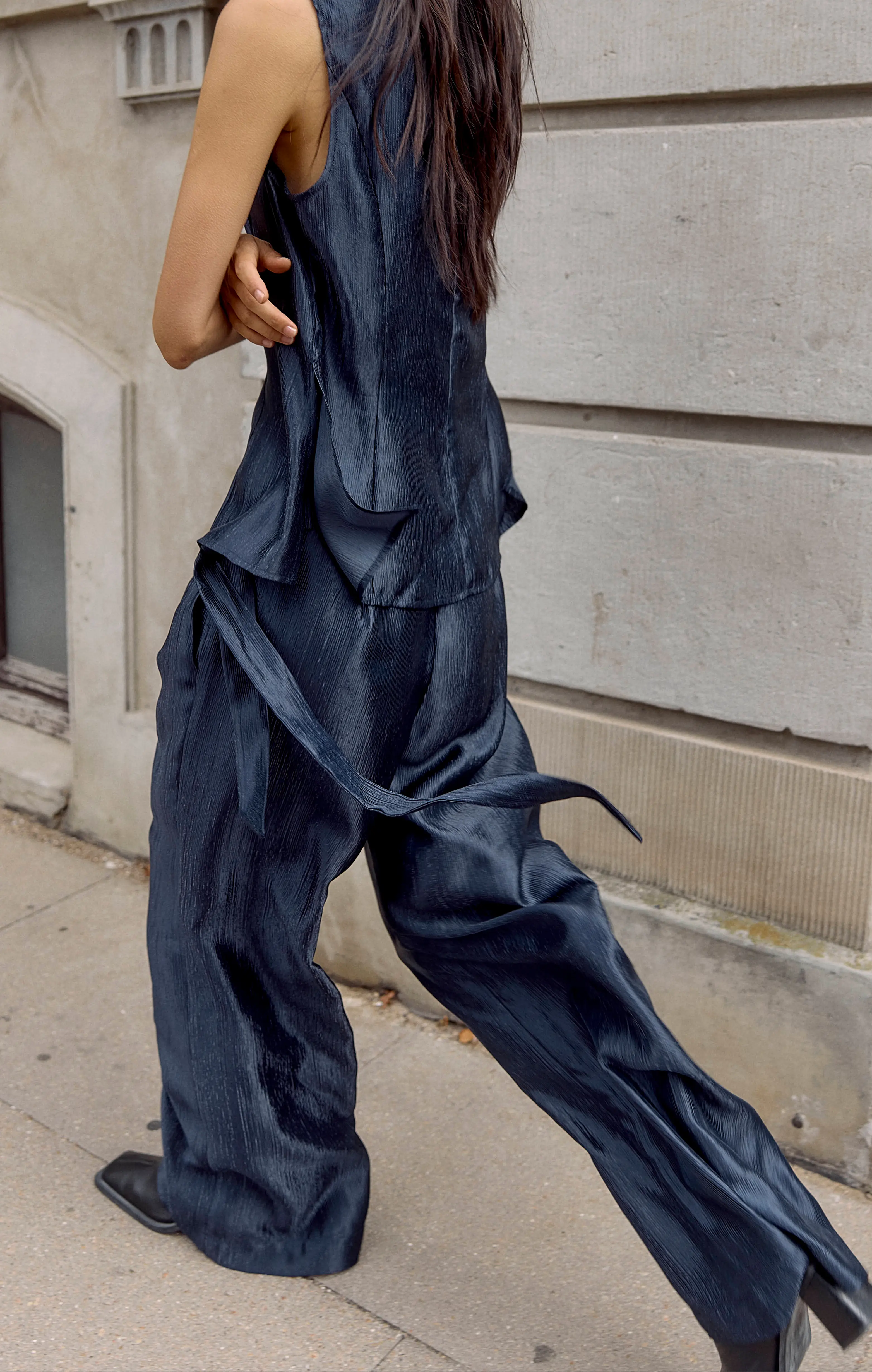Woman in navy sleeveless top and wide-leg pants walking beside a stone wall